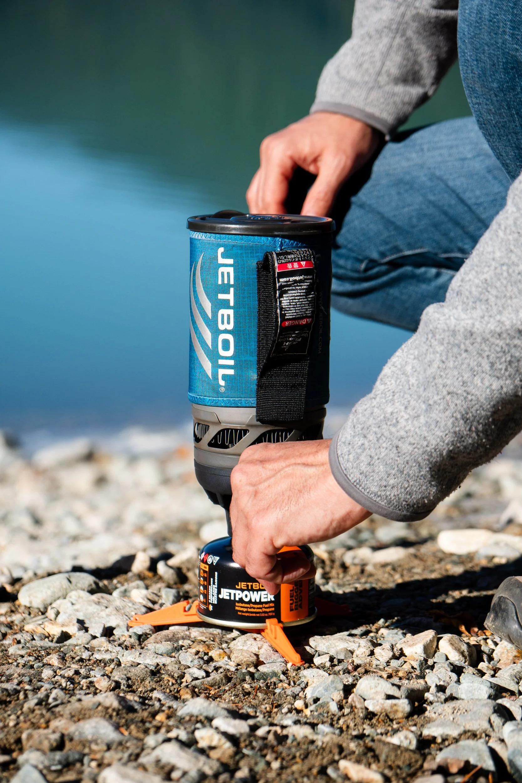 Turning on a jetboil stove in front of a turquoise alpine lake.