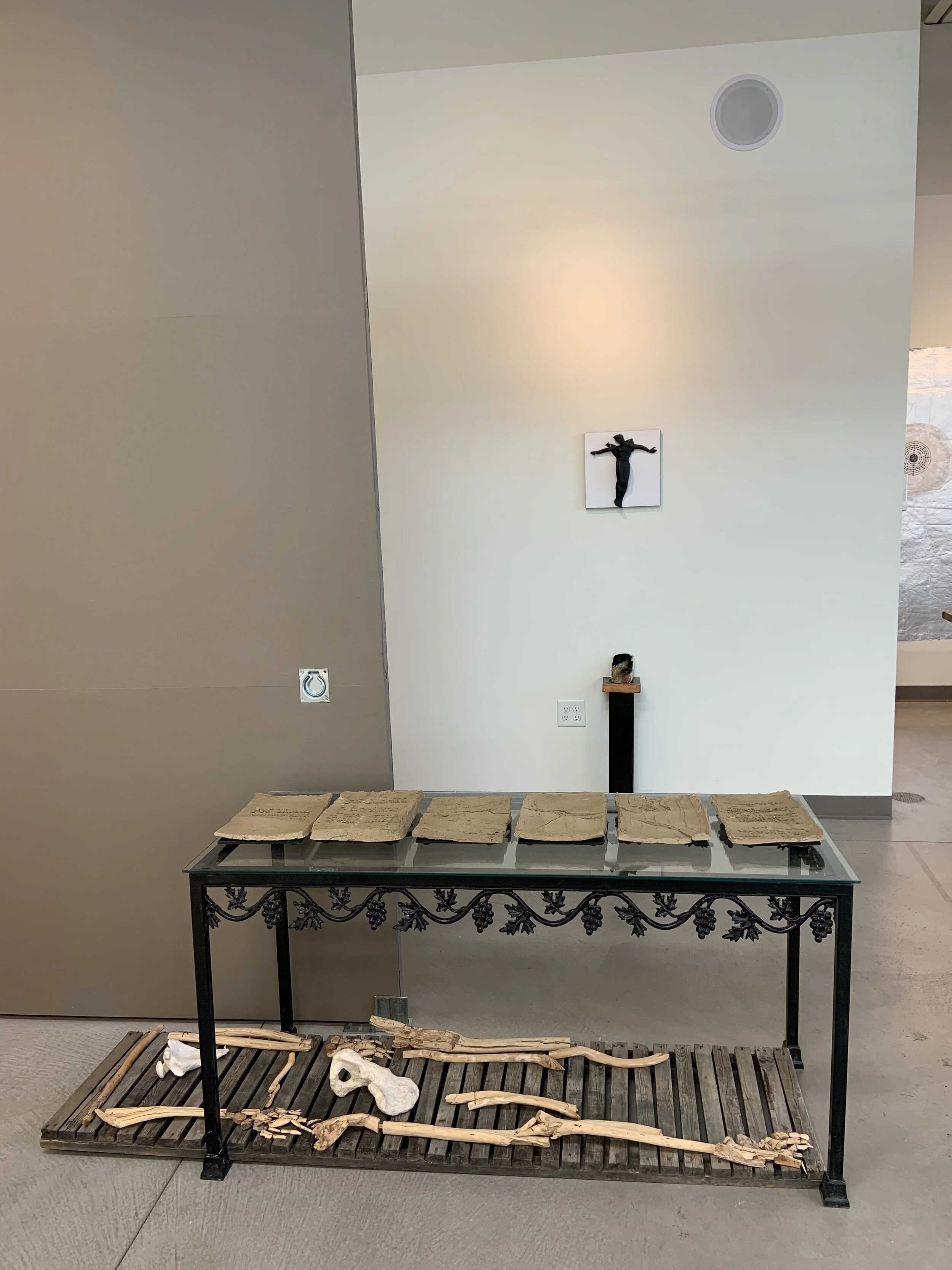 Display of archaeological or fossil artifacts, including stone tablets on a glass table and skeletal remains on a wooden platform, with a sculpture of Jesus on the cross and a small statue on a stand on the wall in the background.