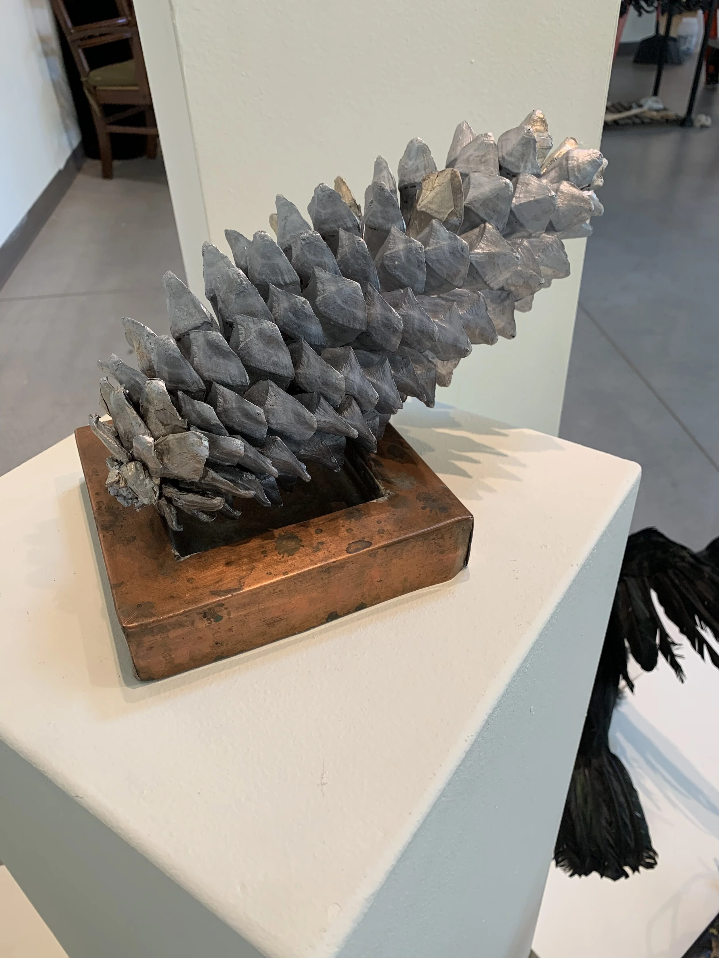 A sculpture of a pine cone made of gray painted material mounted on a wooden base.