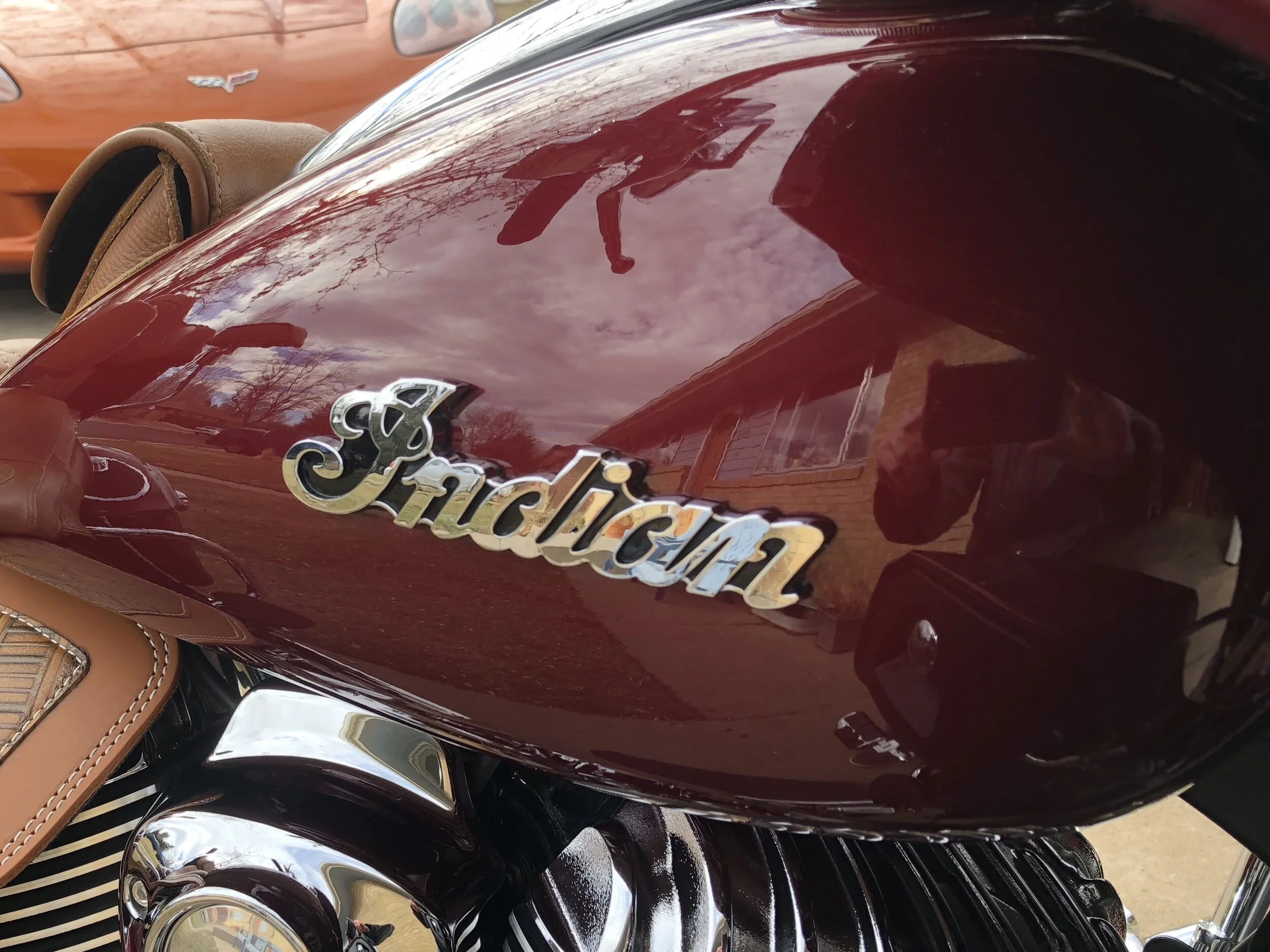 Close-up of a red car with shiny paint, and a badge that reads 'Cindylus', with a tan leather car seat visible at the top left.