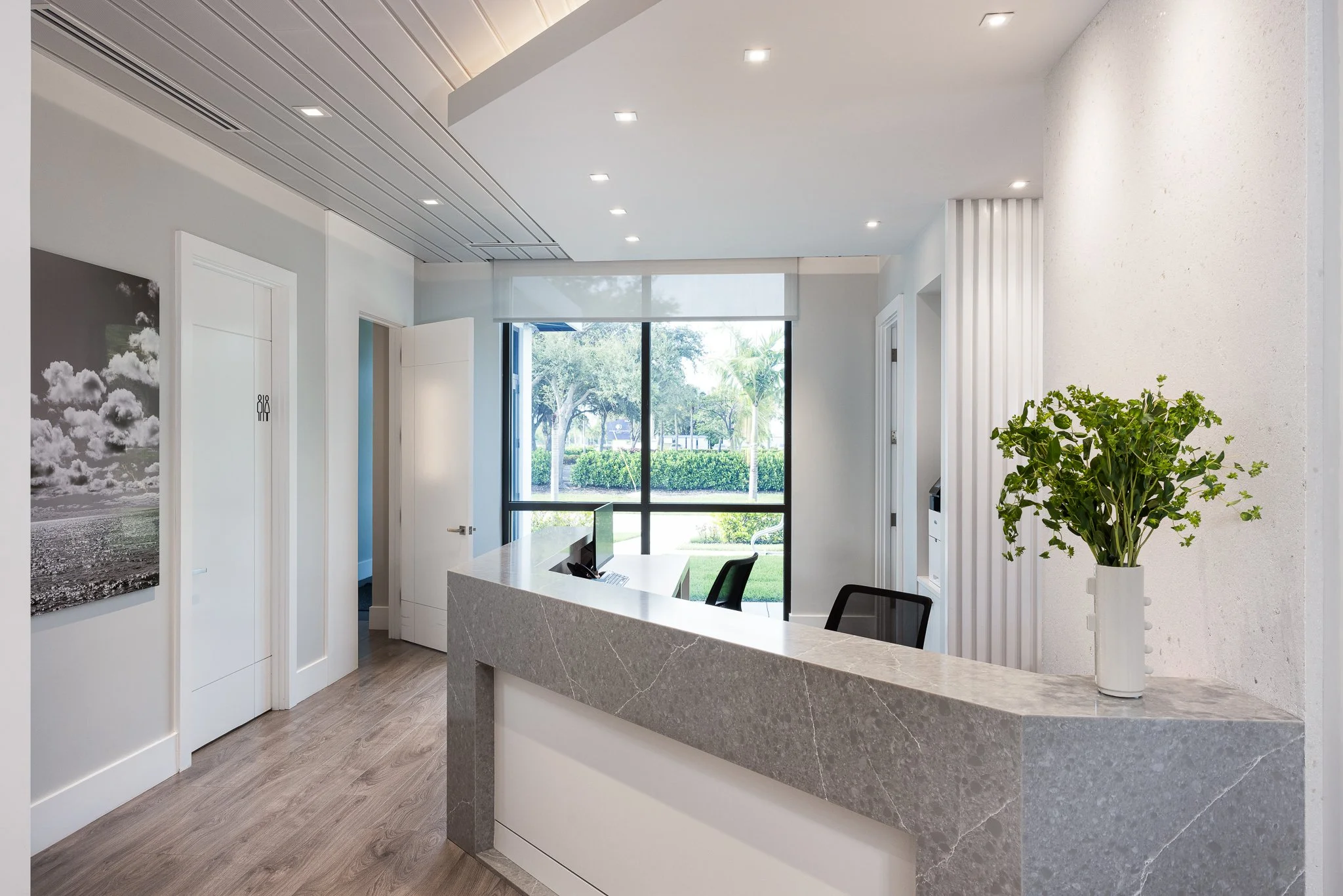 Modern reception area with a curved marble countertop, a potted plant, and a view of trees through large windows.