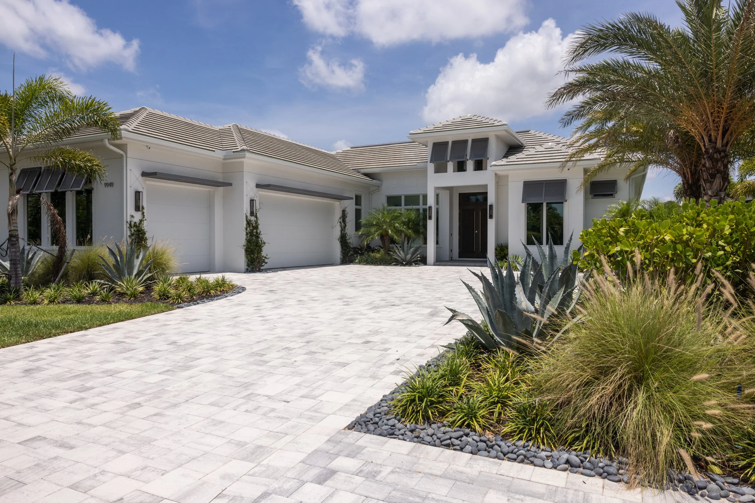 luxury home in naples florida on the golf course. The home is a single story, white stucco with a 3 car garage and paver driveway. The palm trees dot the lush landscape.