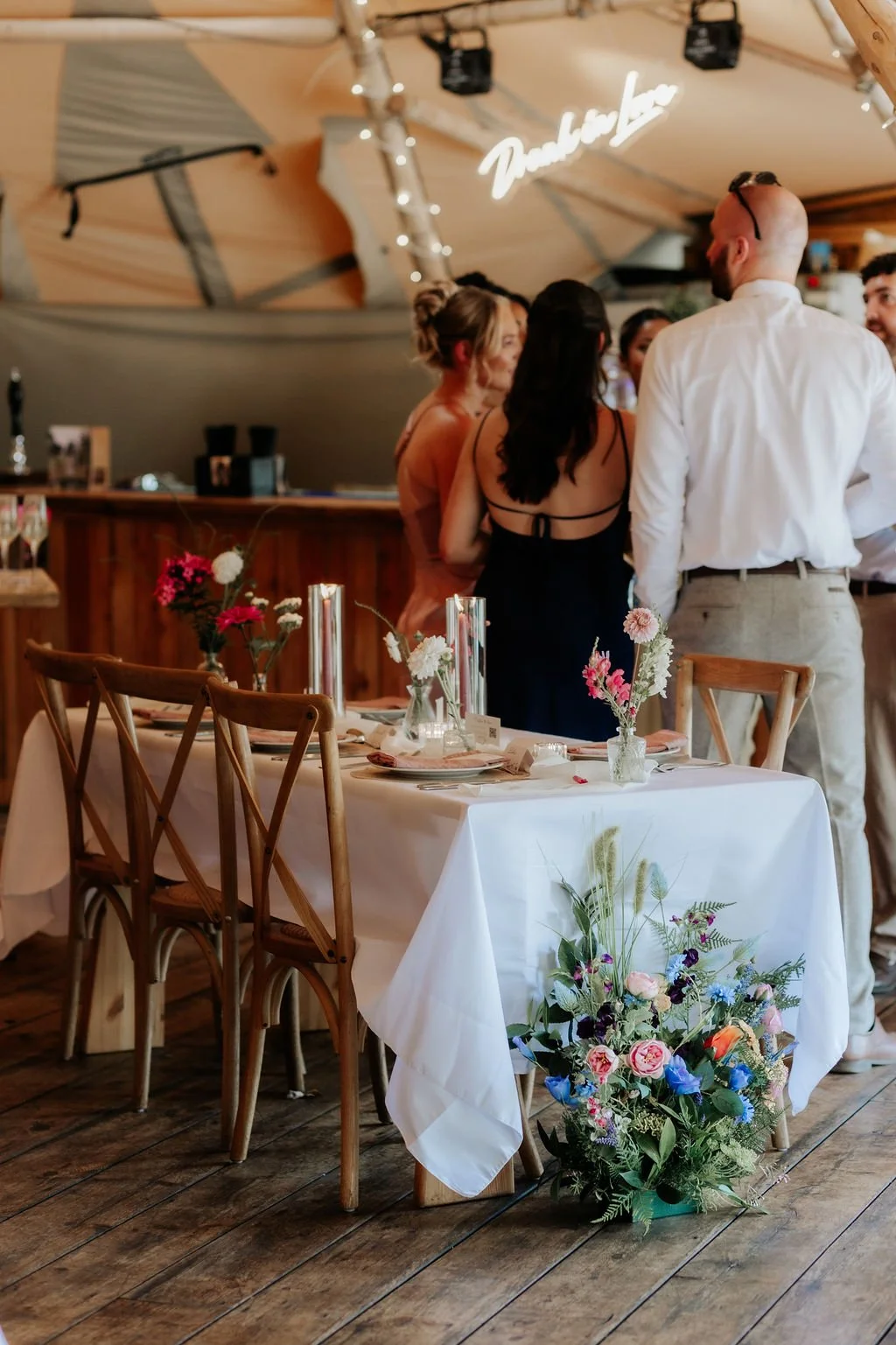 Wedding guests beside a reception table styled with flower bud vases, candles and a colourful arrangement at the table end.