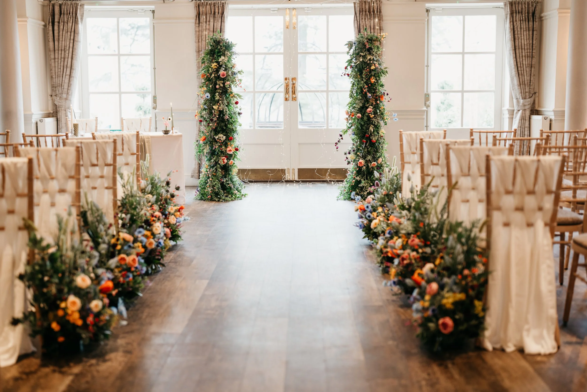 Colourful artificial wedding flower aisle arrangements with statement floral pillars for a wedding ceremony