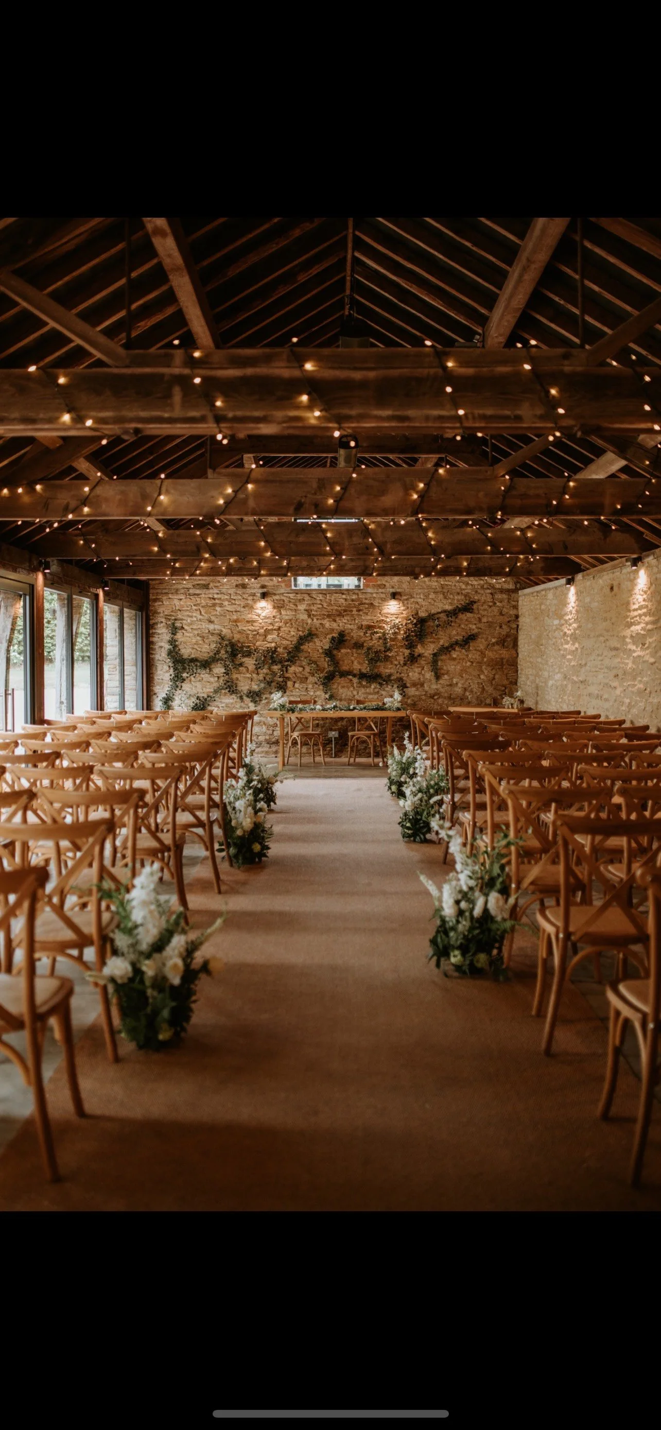 Wedding ceremony aisle styled with artificial floral arrangements in a rustic barn venue