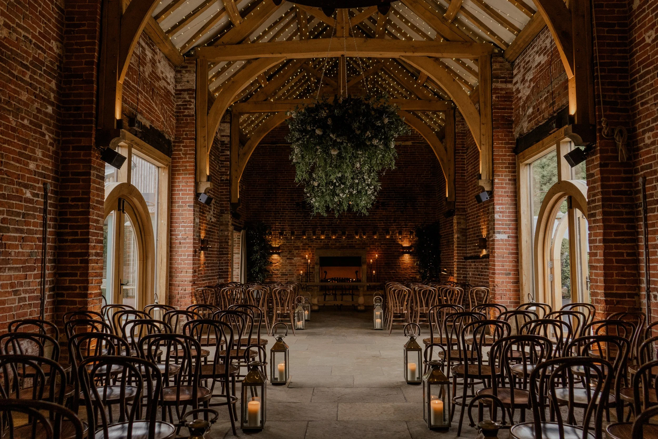 Rustic wedding ceremony at Hazel Gap Barn Nottinghamshire  with candlelit aisle, wooden chairs and statement hanging greenery installation