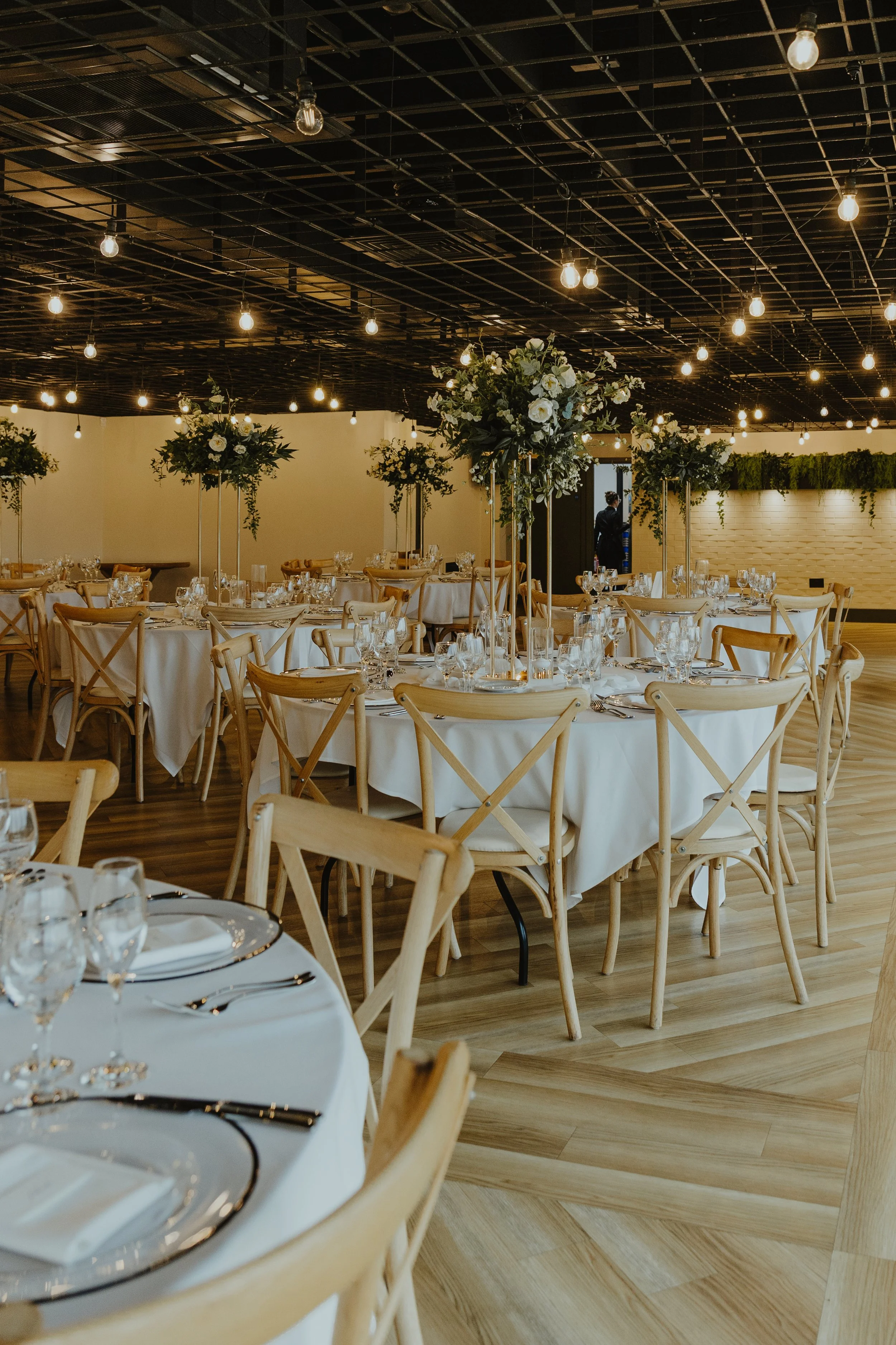 Wedding reception tables styled with tall artificial flower centrepieces and greenery at Whistle Barns