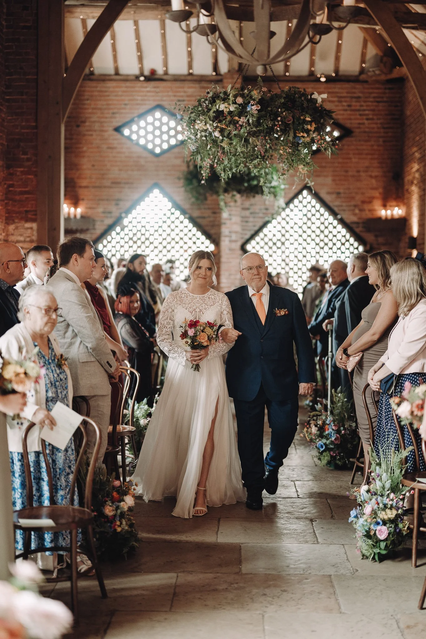 ride walking down the aisle beneath a hanging artificial foliage installation at Shustoke Barn
