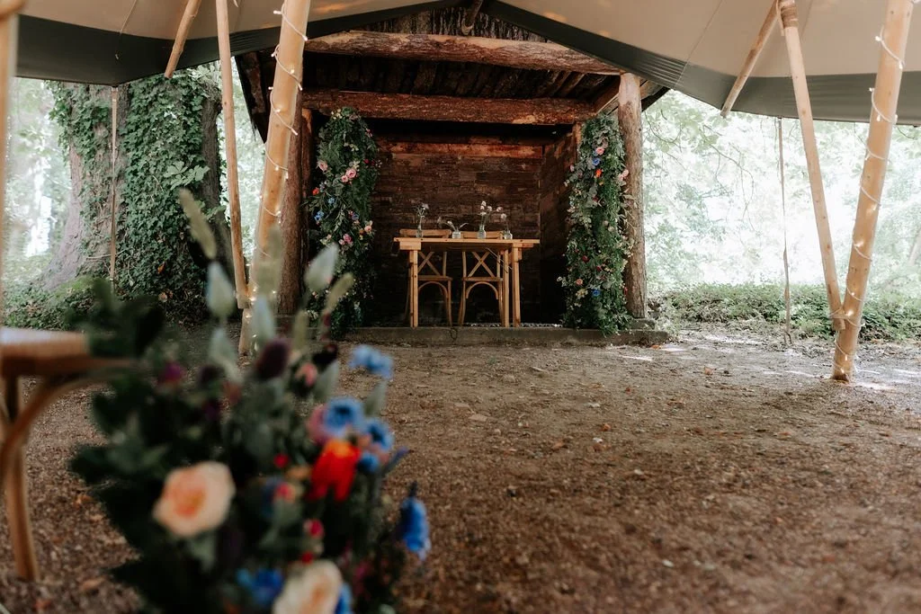 Wedding aisle at Tipis at Whatton House, with colourful flower arrangements leading towards two floral pillars at the ceremony shelter.