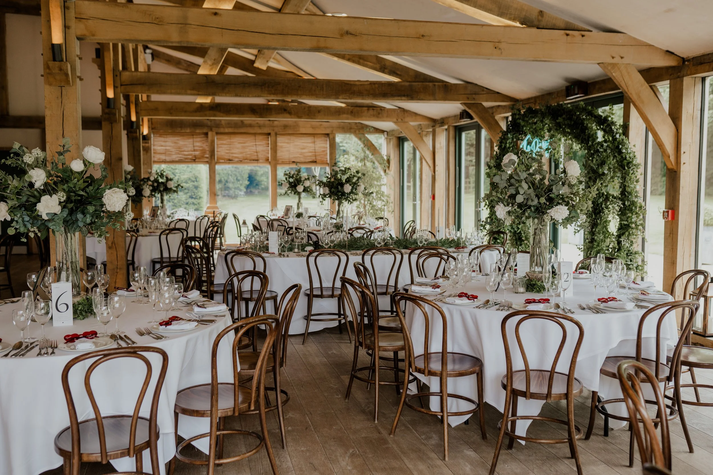Wedding reception tables styled with tall artificial white flower centrepieces and greenery at Hazel Gap Barn, Nottinghamshire