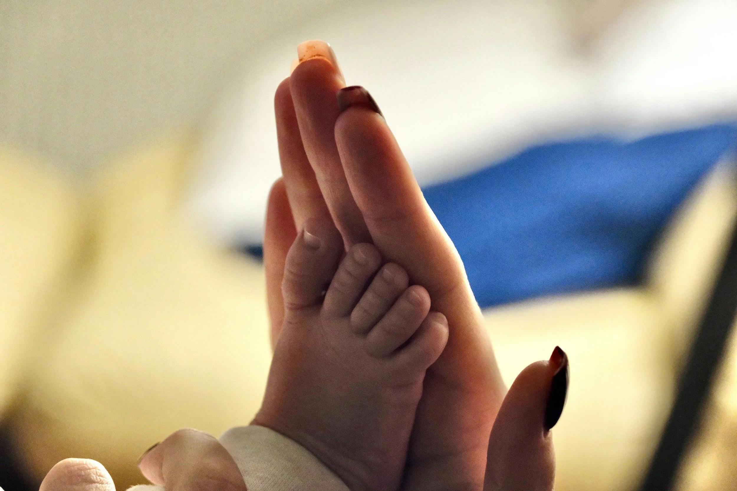 Close-up of adult and baby hands pressed together with fingers extended, showing contrast in skin tones and nail polish.