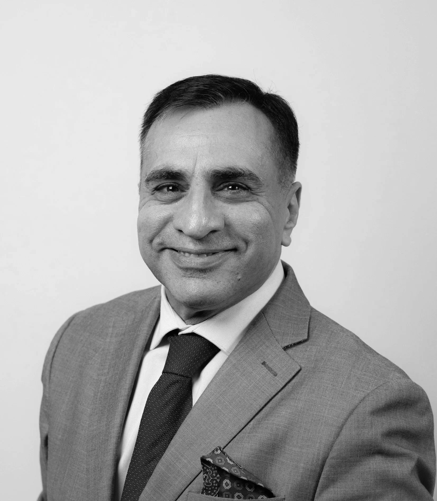 Black and white photo of a man with short dark hair, smiling, wearing a suit and tie.
