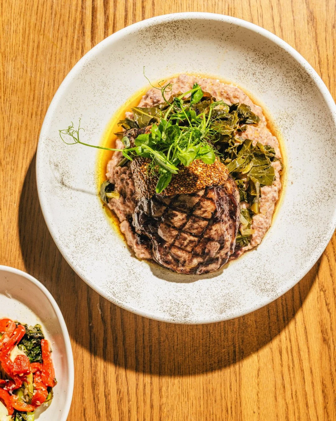 There's something deeply satisfying about a pork chop done exactly right. Sweet tea brine, BBQ glaze, pimento cheese grits, collard greens, a beautiful pickled mustard &mdash; our spring update of the @peculiarpigfarm Pork Chop is Eastern North Carol