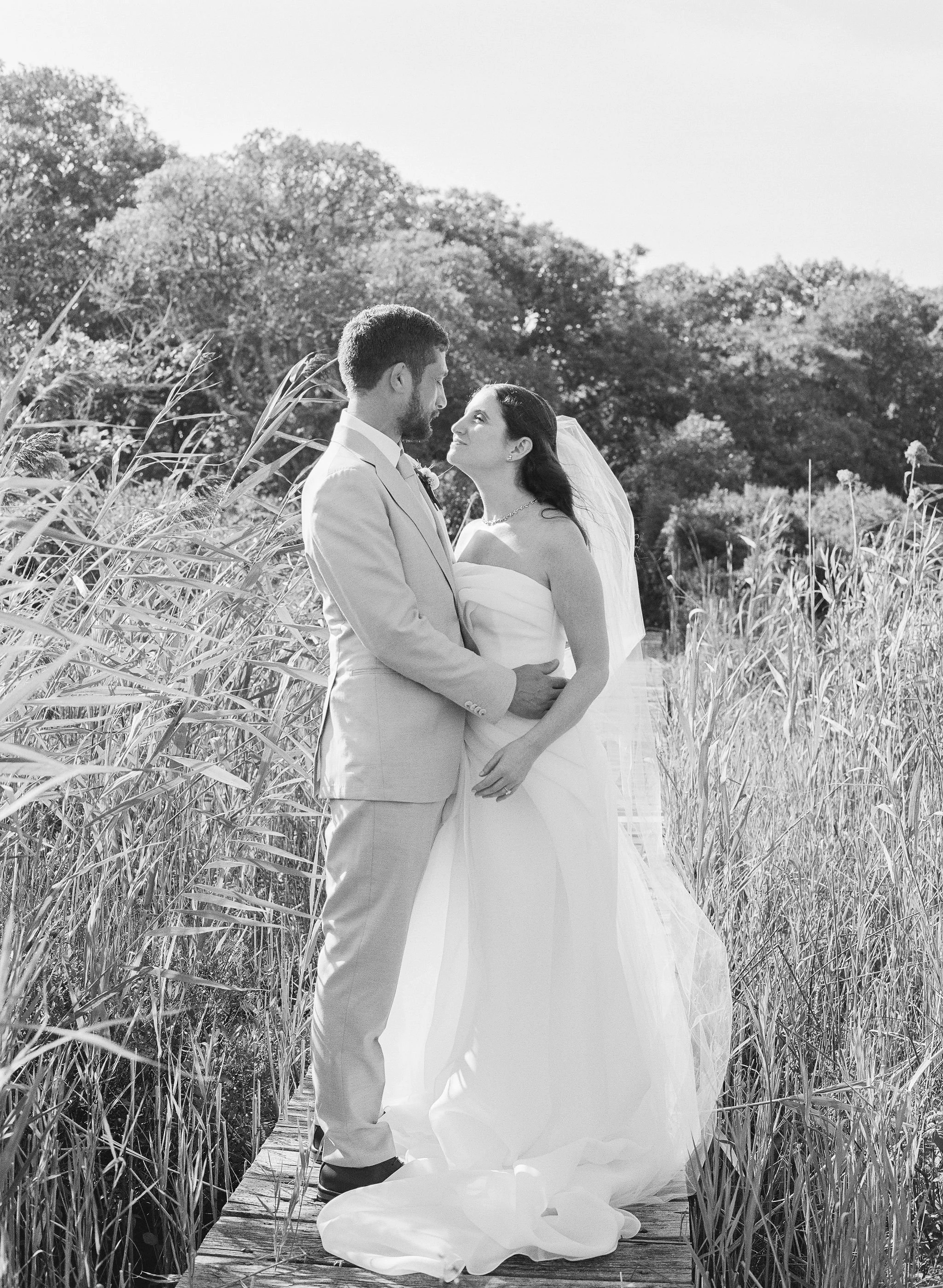 A couple gazes affectionately into each other's eyes during their first look on the brides family's dock on Edgartown Great Pond. Tall marsh grass surrounds them and a pastoral oak vista frames the background