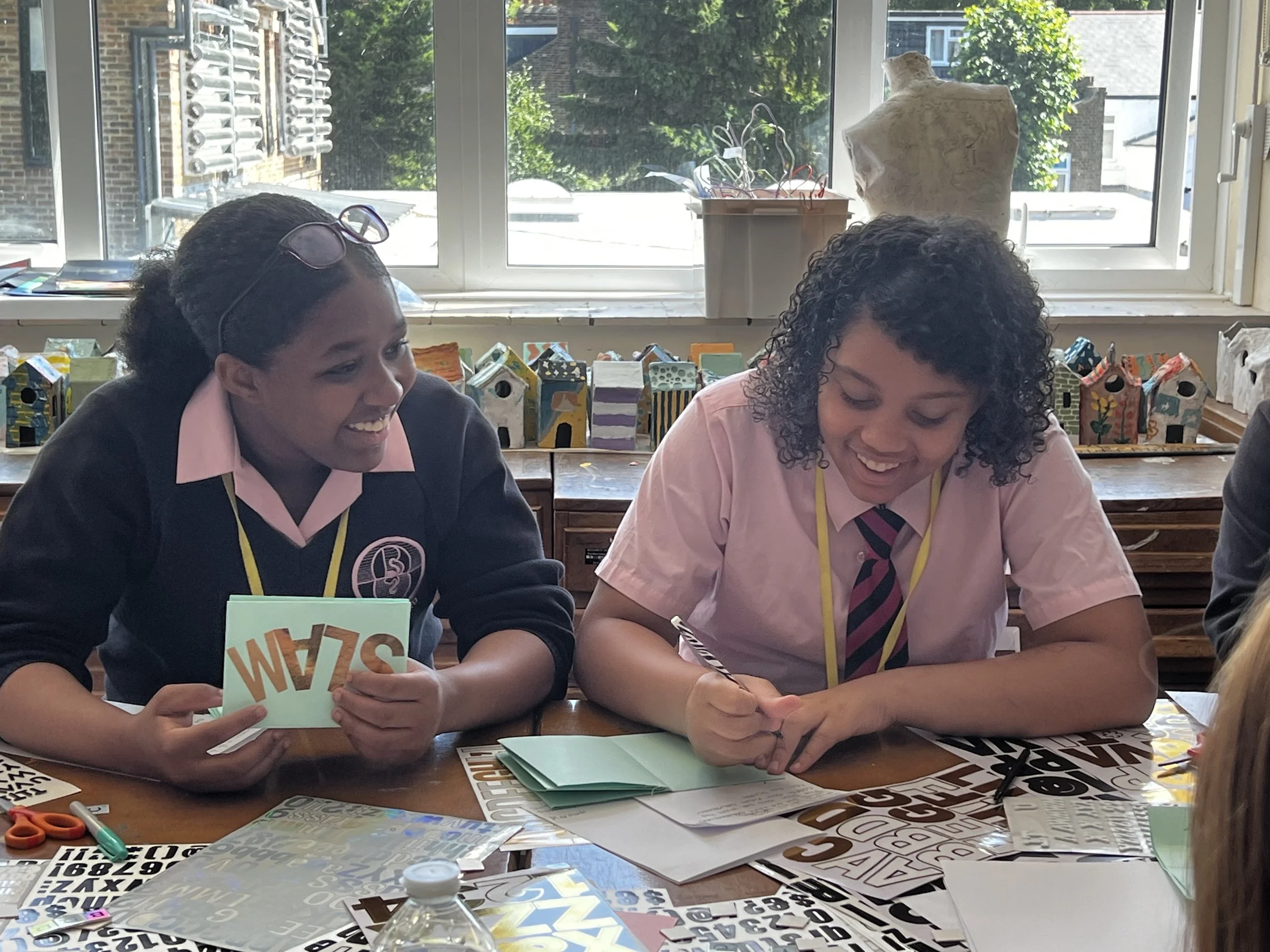 Two young people laughing whilst making zines surrounded by art materials