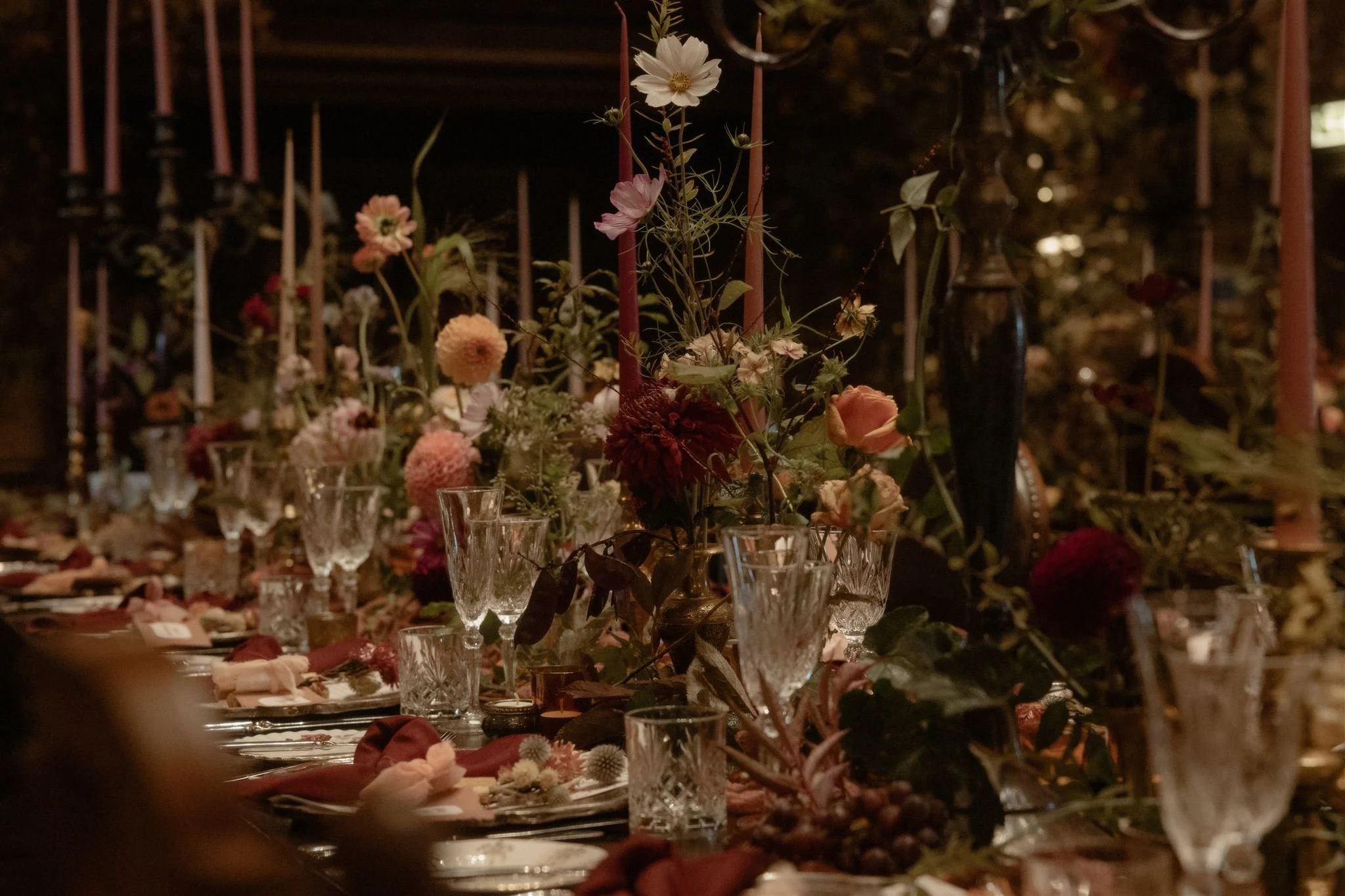 A dimly lit indoor celebration with floral centerpieces on a decorated table.