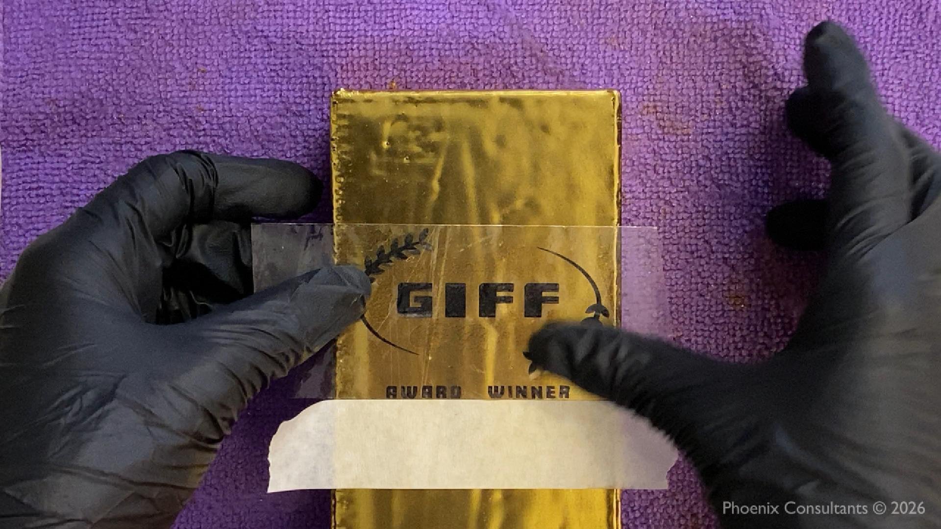 Image taken from the behind the scenes video of making a GIFF003 gold award. Image features application of the GIFF Award Winner logo onto the finished gold bar created by Phoenix Consultants.