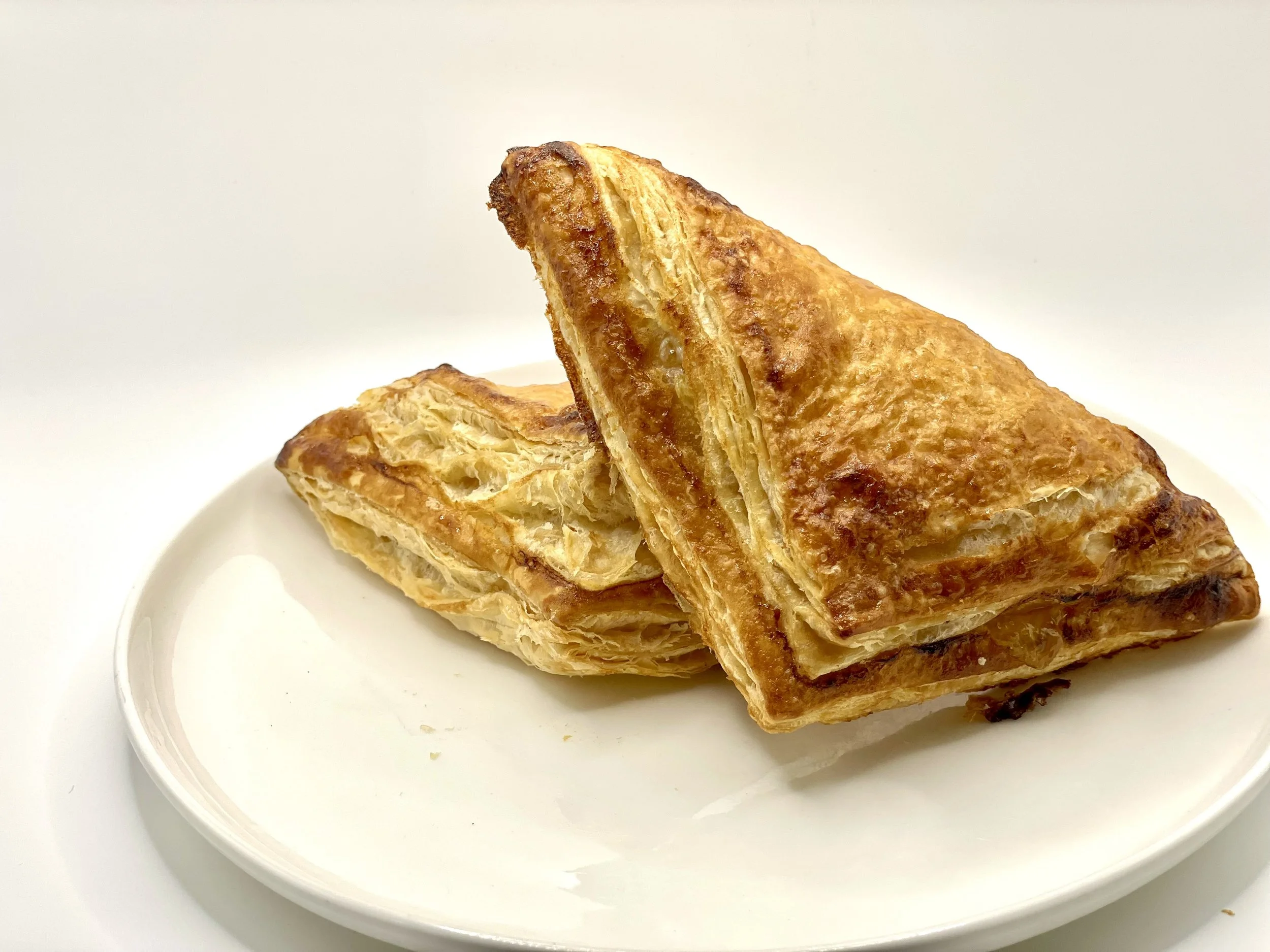 Close-up of two pieces of fried puff pastry on a white plate with a plain white background.