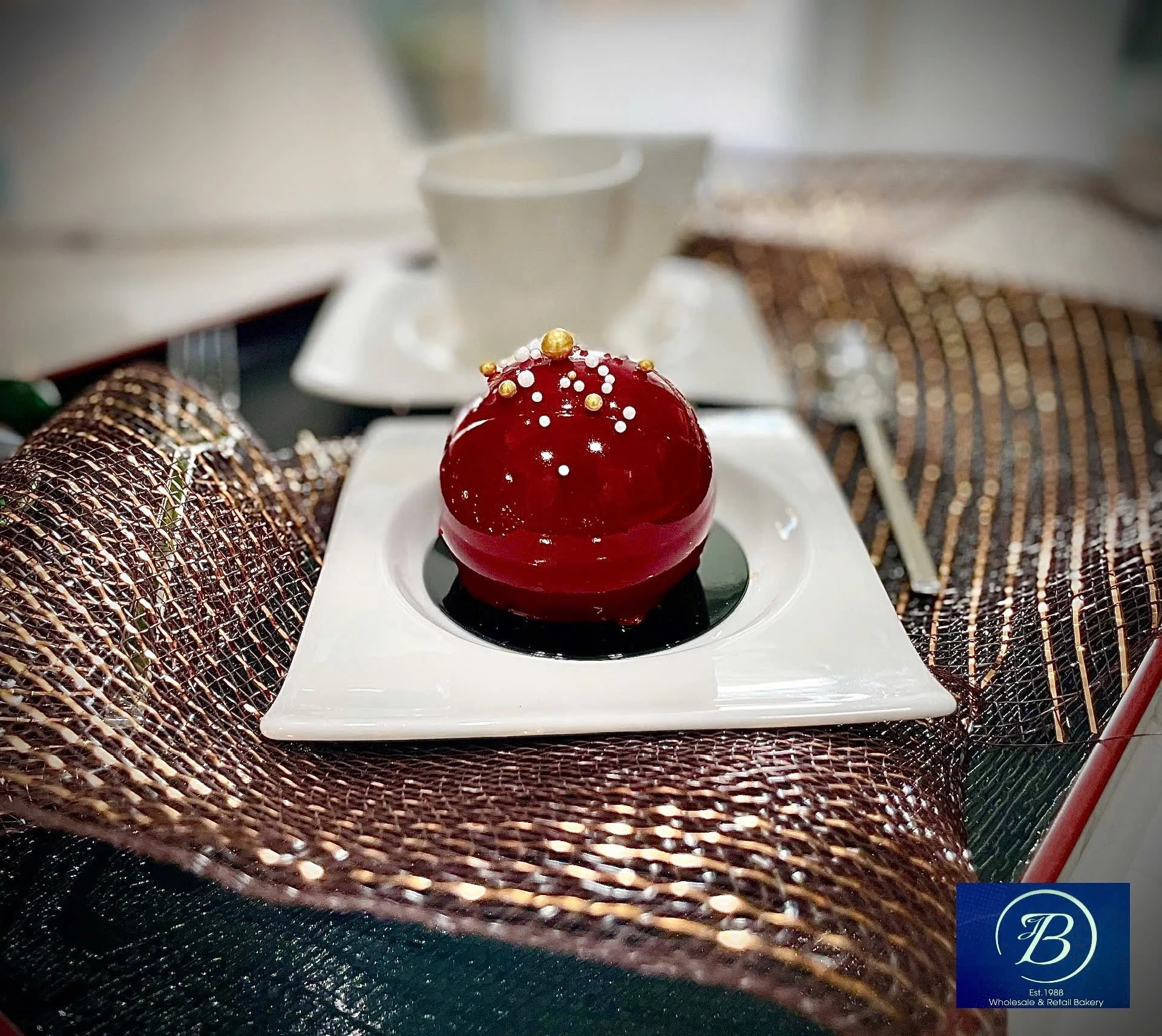 A red, dome-shaped dessert decorated with white and gold sprinkles on top, placed on a white plate