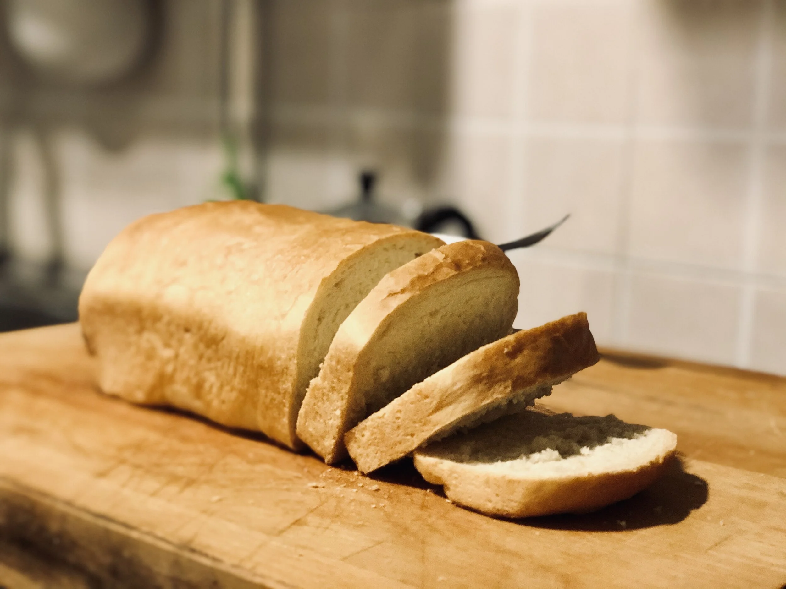 Slices of bread on a wooden cutting board, with a textured white wall in the background.