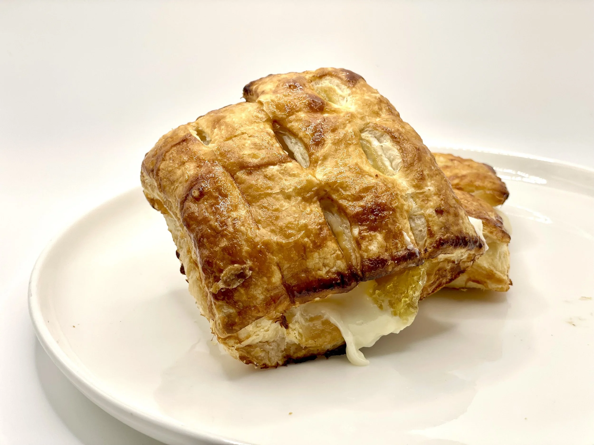 Close-up of a baked, crispy pastry filled with cheese on a white plate.