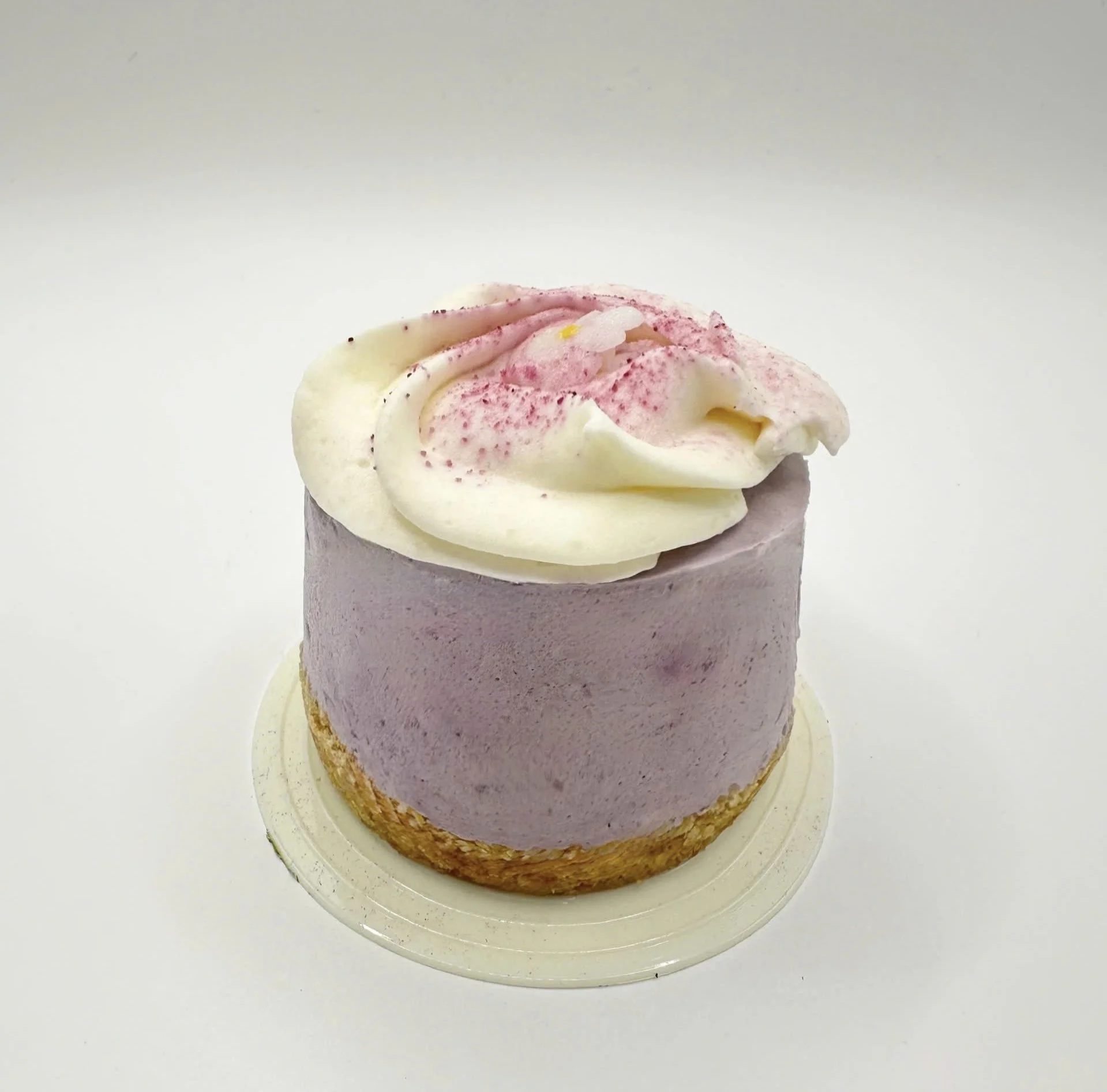A cupcake with white and pink frosting topped with sprinkles, placed on a clear glass plate against a plain white background.