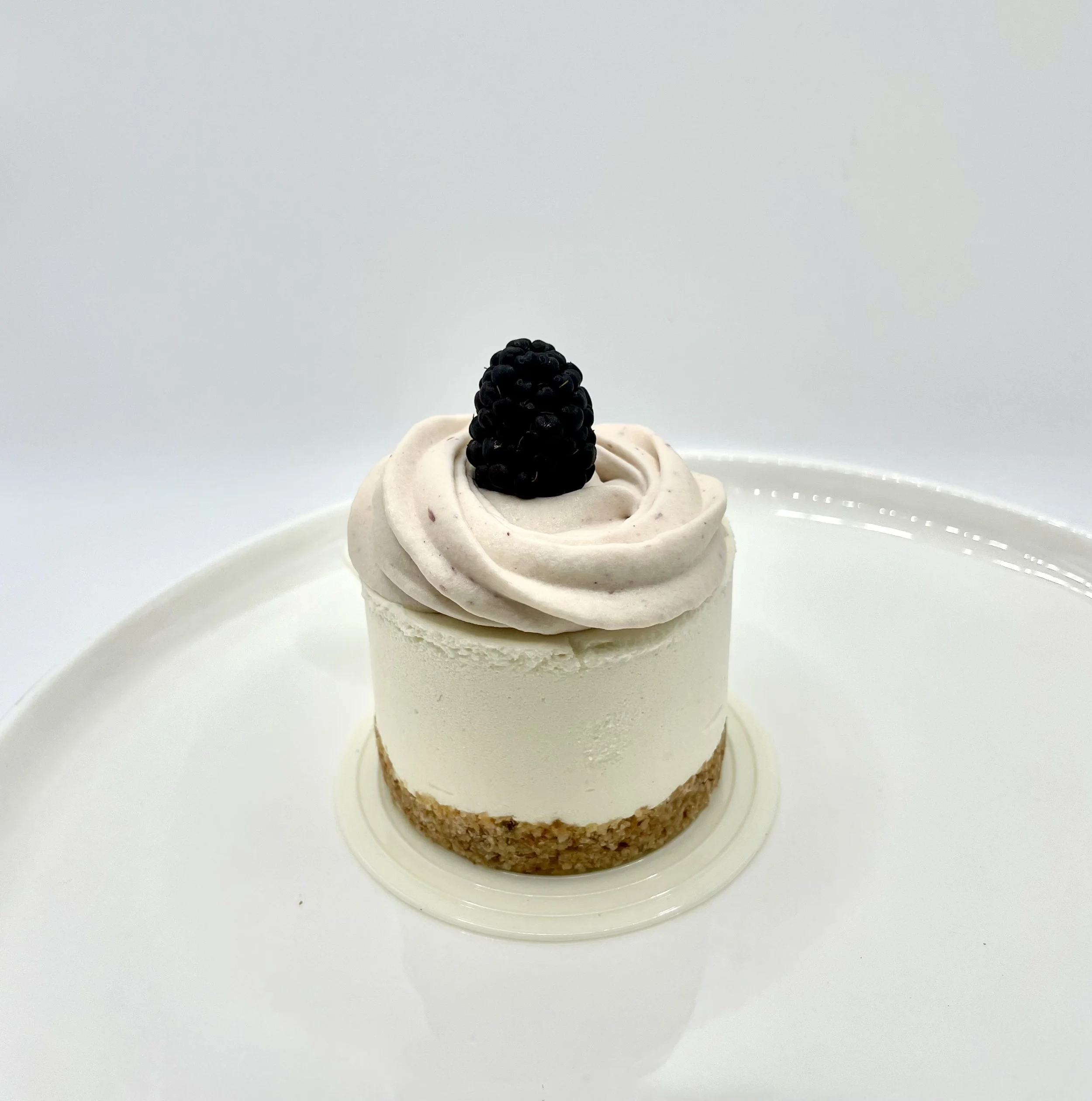 A dessert with a cookie base, topped with white whipped cream or mousse and garnished with a single blackberry on top.