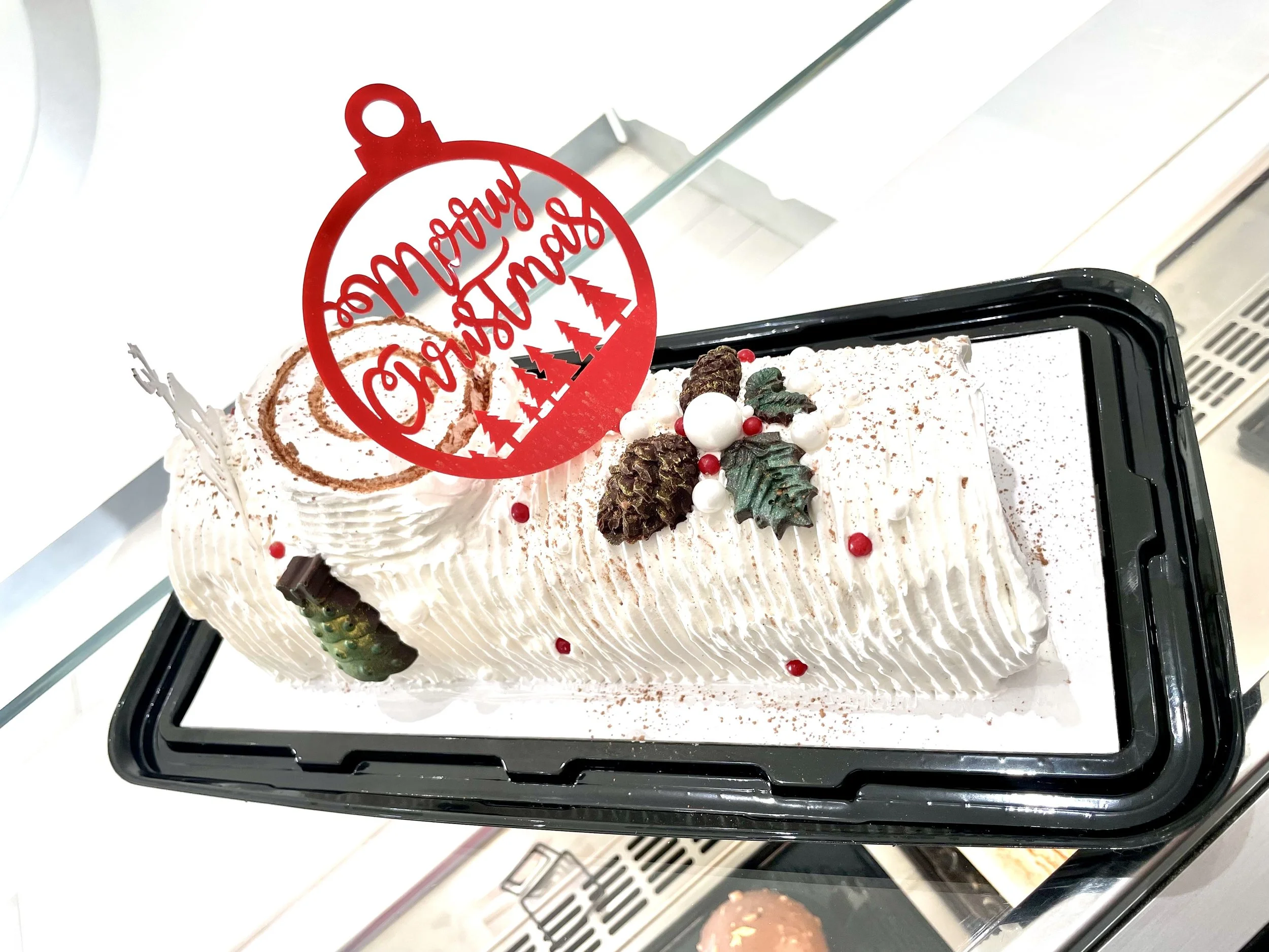 Christmas cake decorated with candies, holly leaves, pinecones, and a red ornament-shaped topper that says "Merry Christmas."