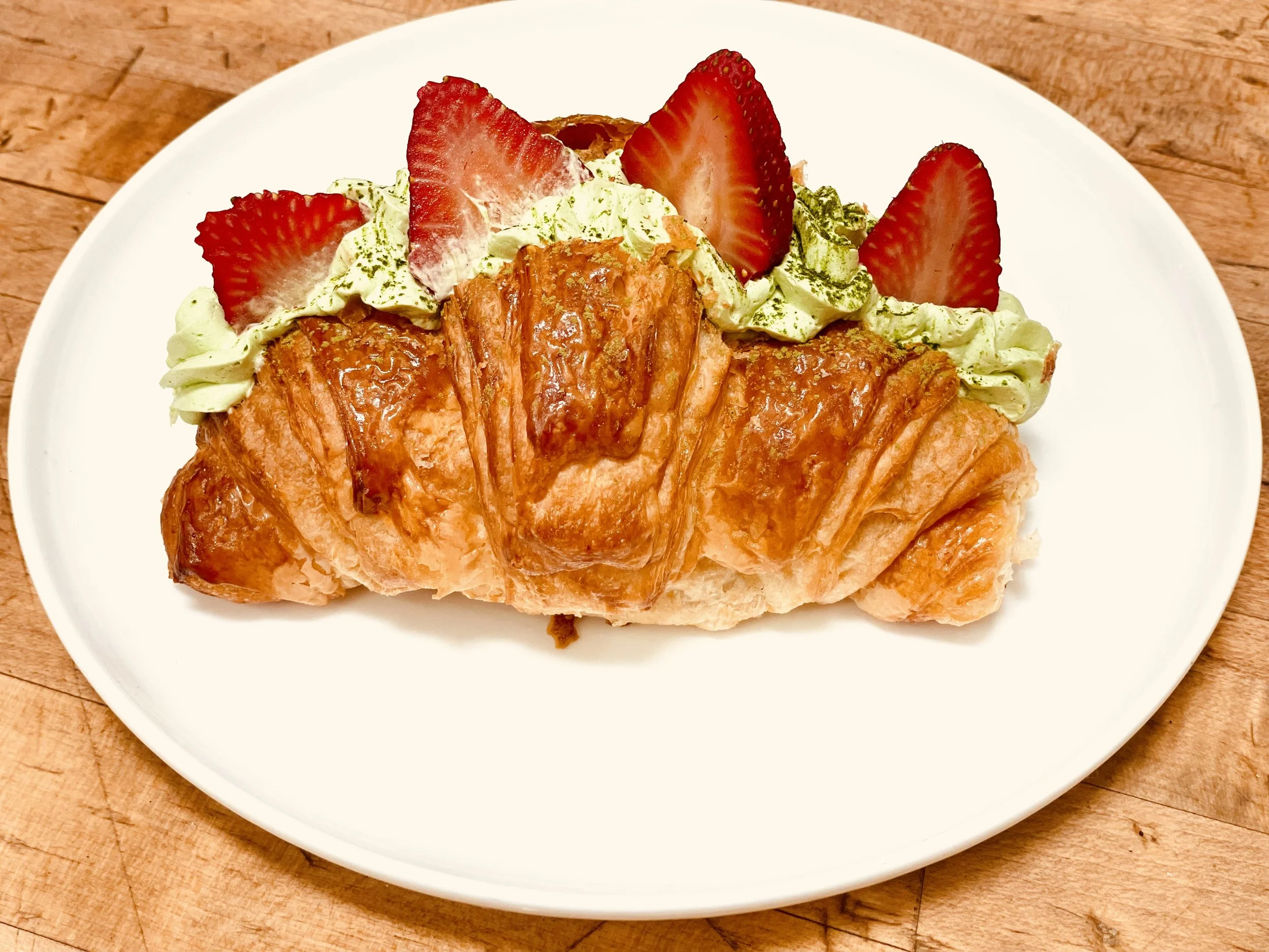 Our Matcha Strawberry Butter Croissant features a golden, delicately flaky butter croissant filled with smooth, creamy matcha cream and beautifully finished with slices of fresh strawberry—a perfect balance of rich buttery flavor, earthy matcha, and 
