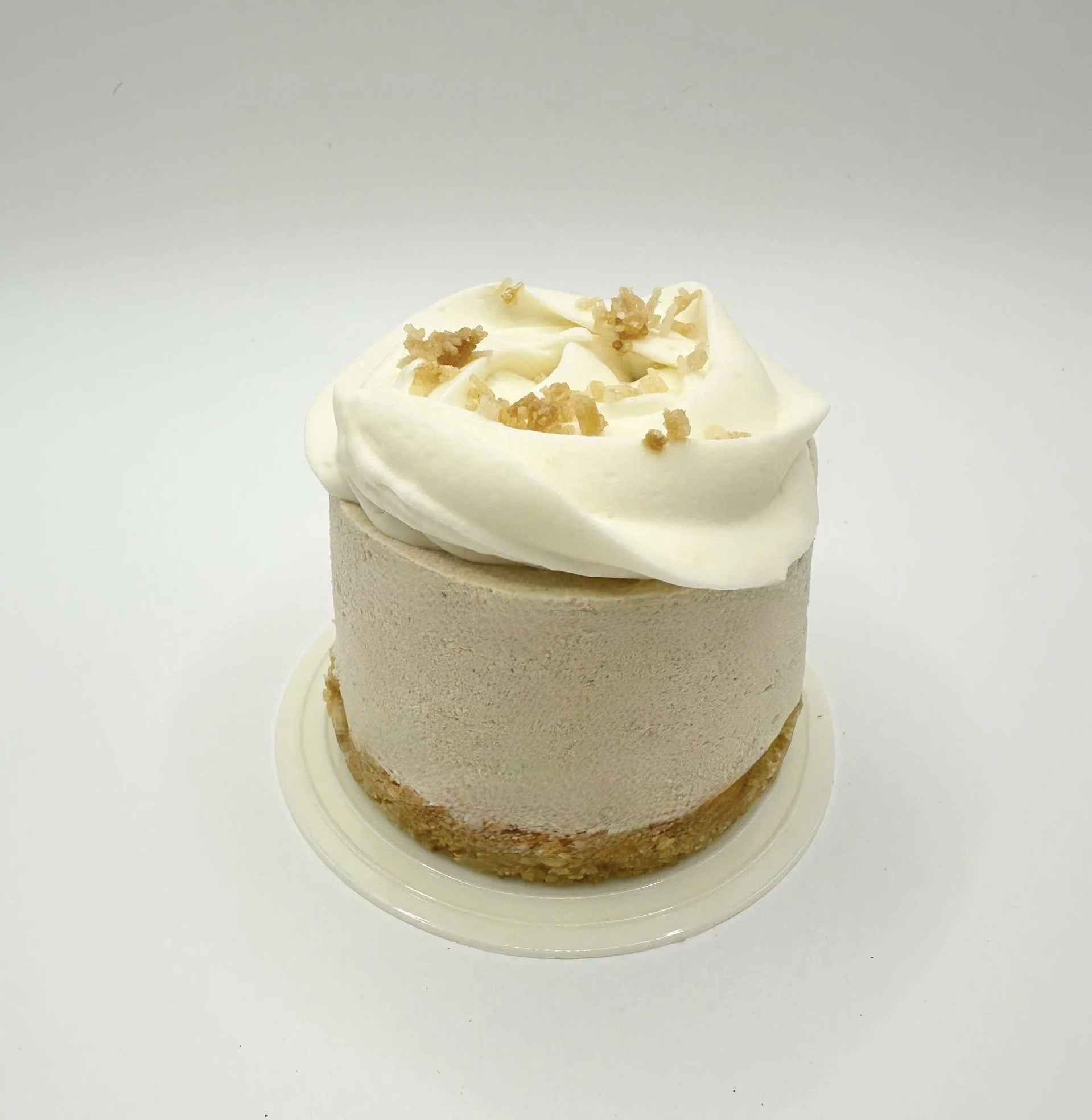 A small round dessert with creamy white frosting topped with crumbled biscuit pieces, placed on a clear plastic tray.