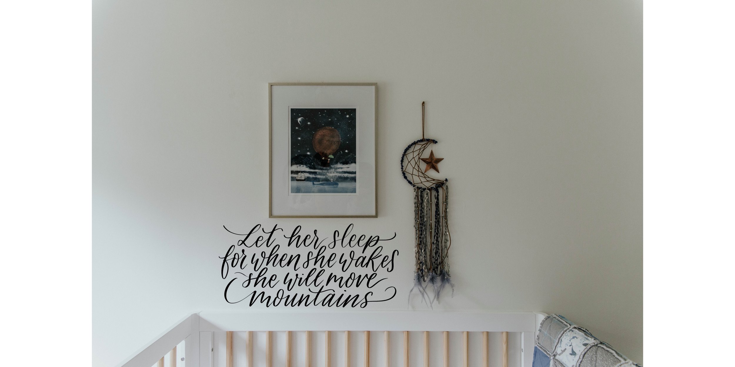 Nursery wall decor with framed picture, crescent moon dreamcatcher, and "Let her sleep for when she wakes she will move mountains" quote above a crib.
