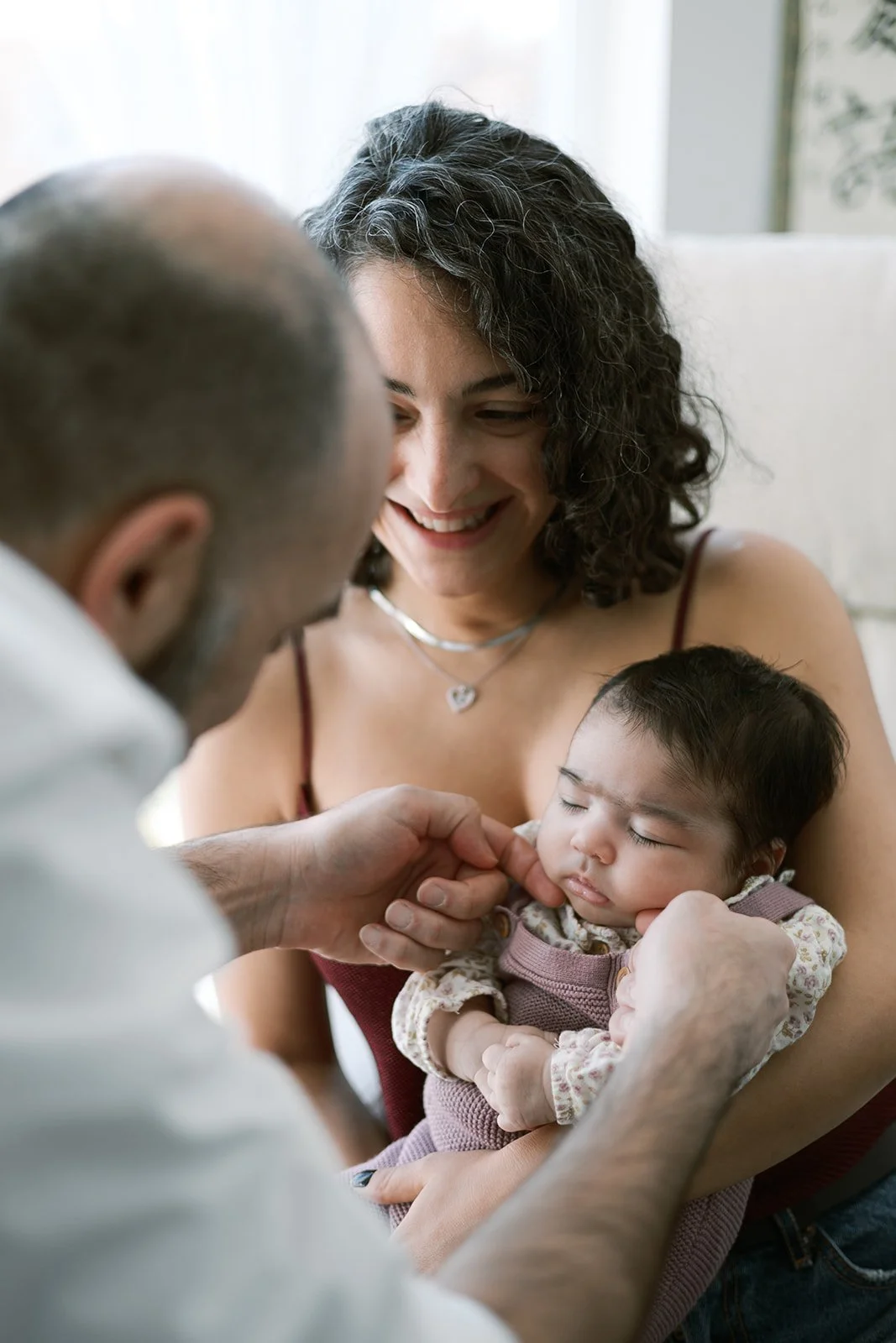 A woman happily holds a sleeping baby while a man gently touches the baby's cheek.