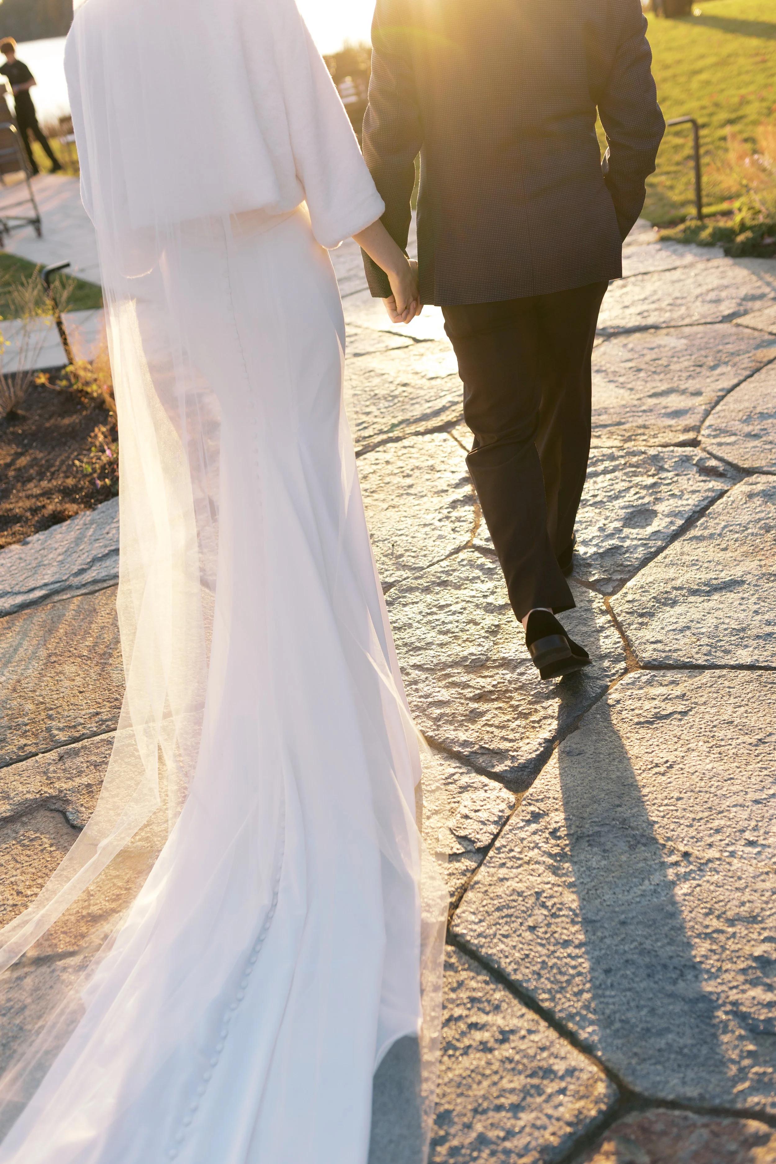A bride and groom holding hands while walking on a stone path outside at sunset during their wedding.