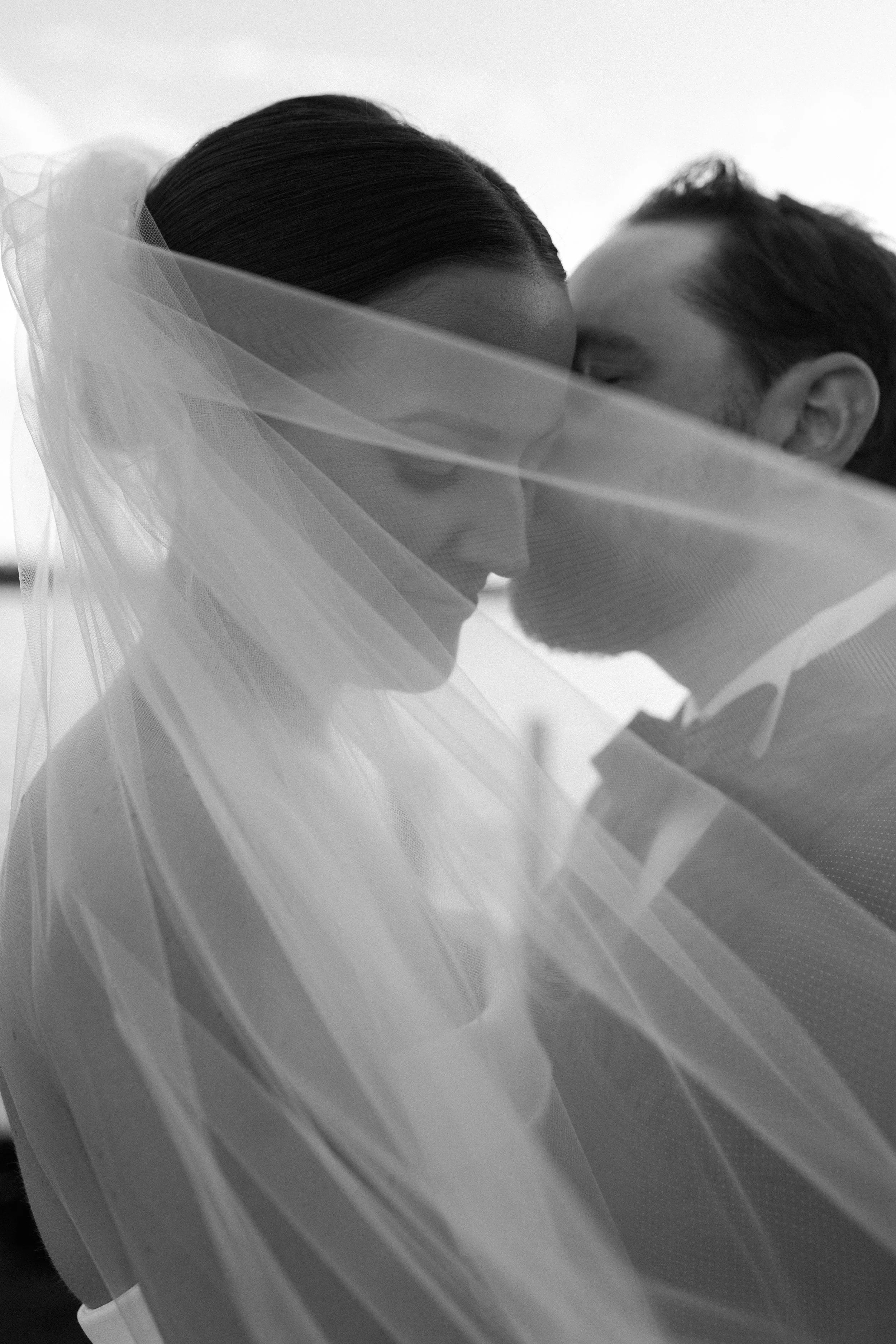 A black-and-white photo of a bride and groom with their faces close, partially obscured by the bride's veil.