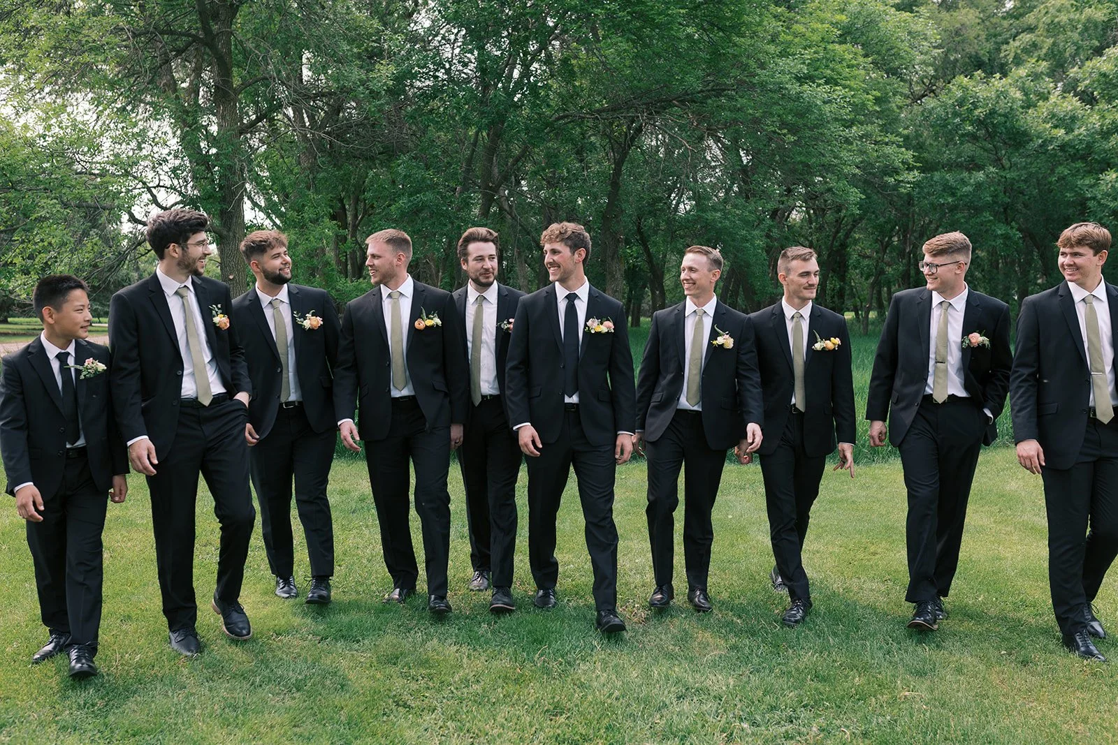 A group of men in formal suits walking together outdoors with green trees in the background.