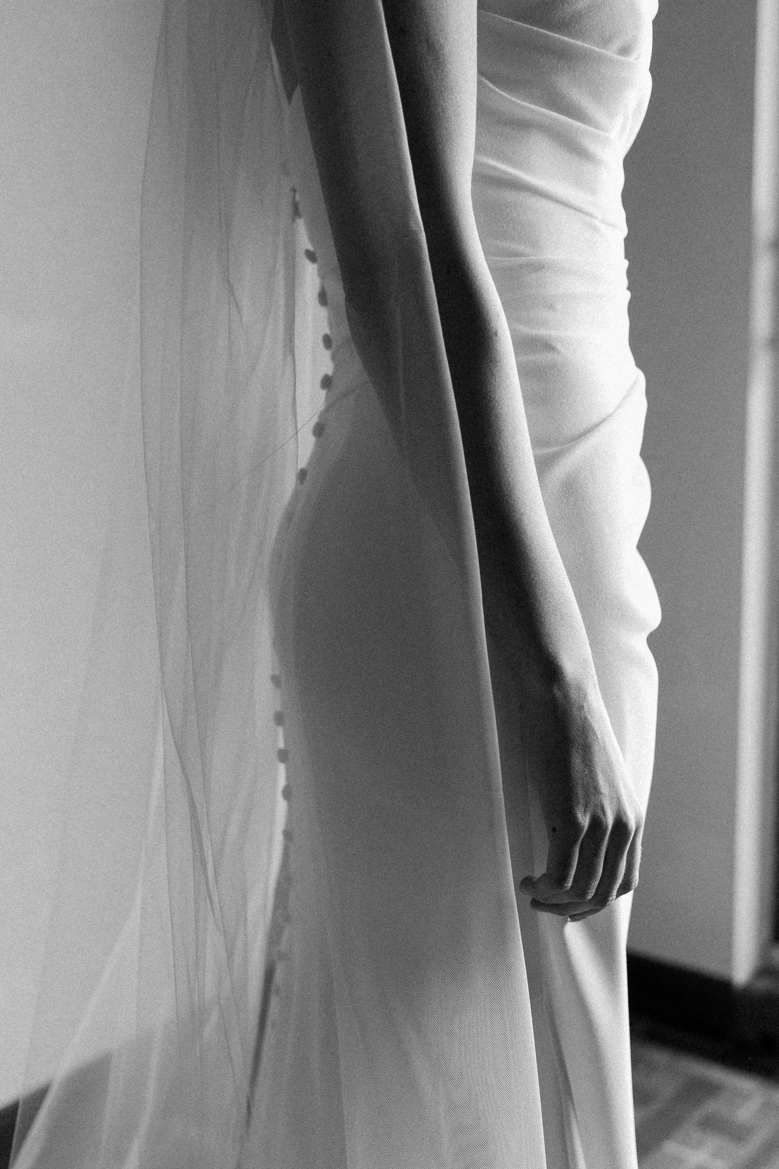 Close-up of a person in a wedding dress, showing the fitted bodice, part of the skirt, and the person's hand hanging down.