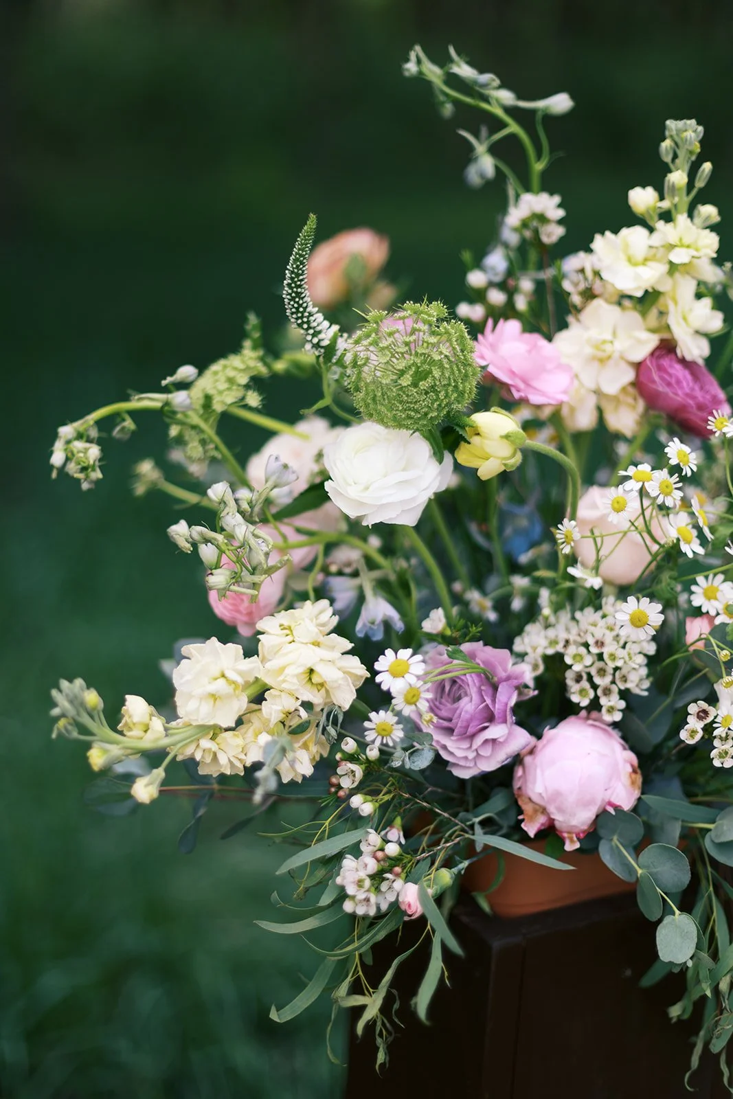 A bouquet of various flowers, including pink, white, and purple blooms, with greenery, in a container outdoors against a green grass background.