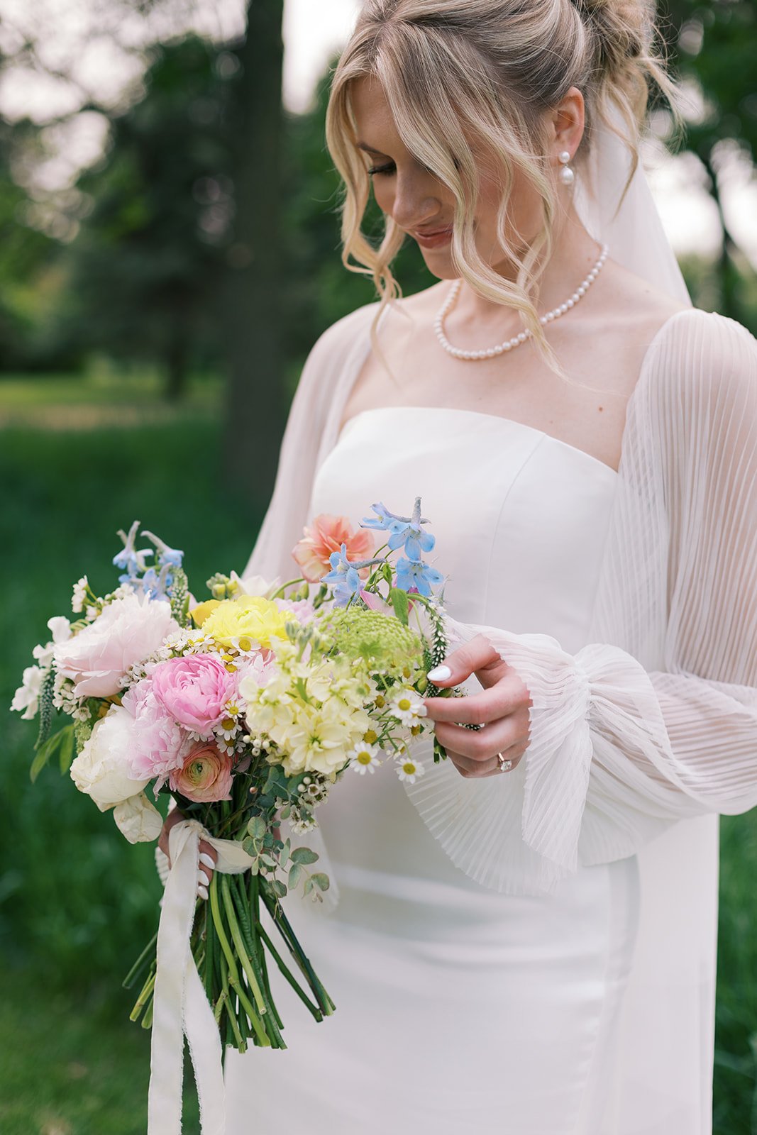 Bride in white dress holding a colorful bouquet of flowers outdoors.