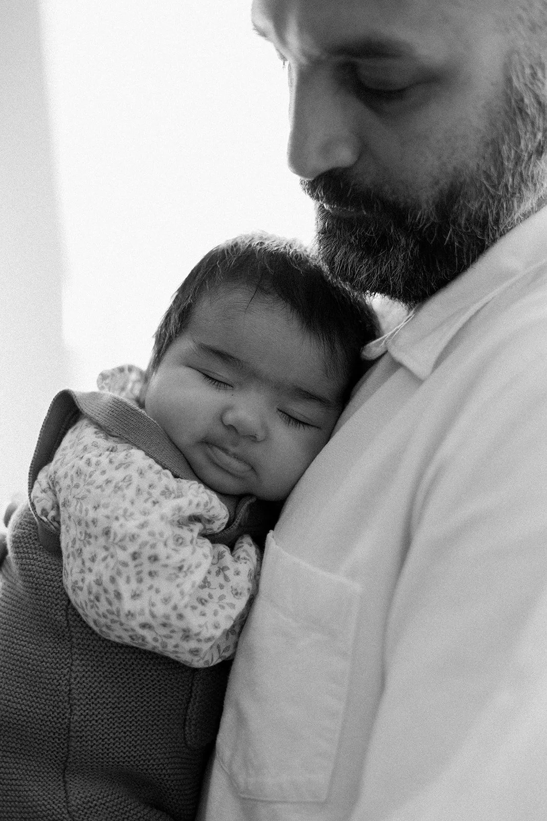 A black-and-white photo of a young child sleeping peacefully on an adult's shoulder, with their eyes closed and a gentle expression.