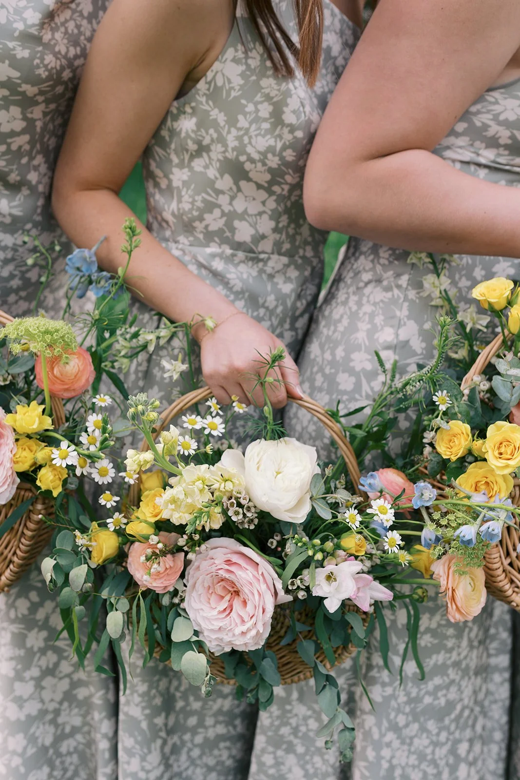Two women in floral dresses holding baskets of colorful flowers.
