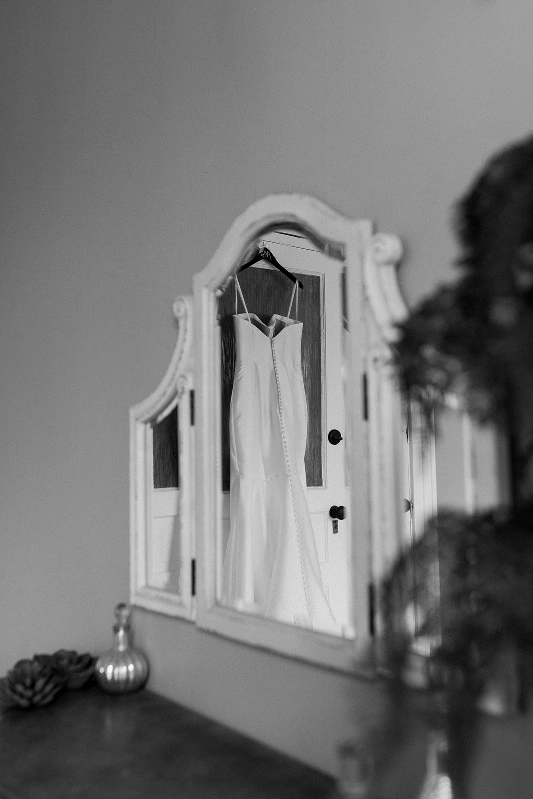 A wedding dress hanging on a hook in front of a mirror, reflected in the mirror, on a wooden door.