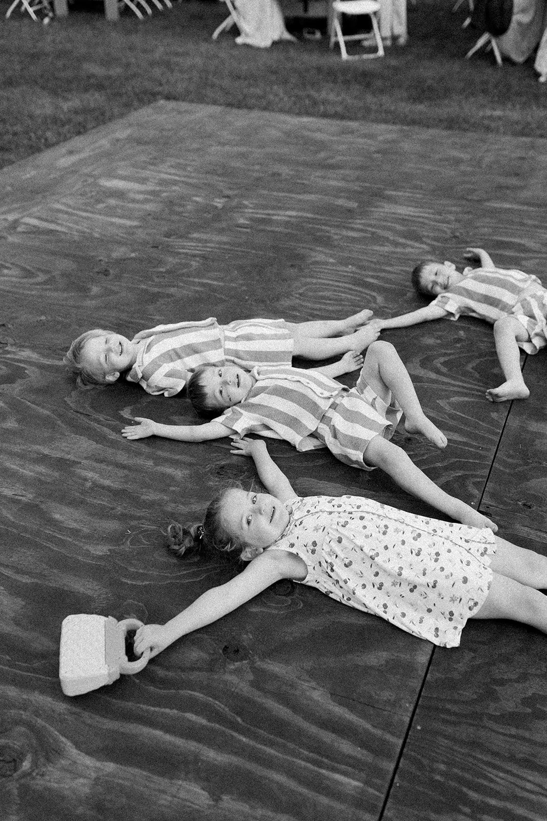 Four children lying on the floor with striped and patterned clothing, holding hands, in an indoor setting.