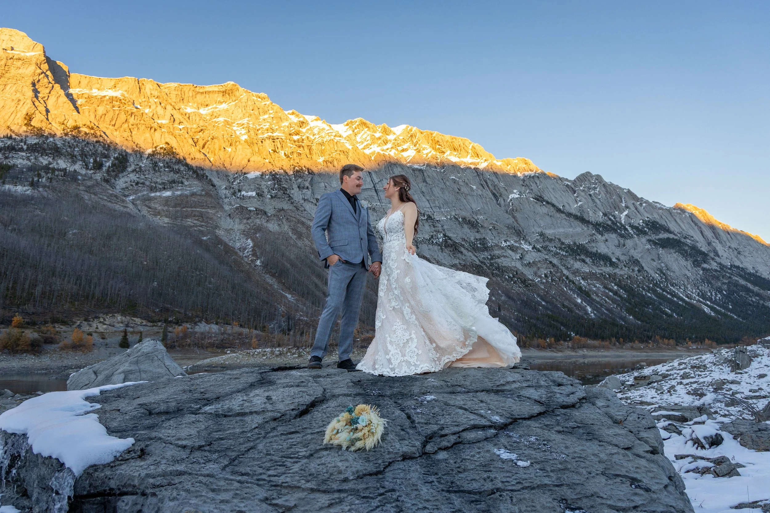 A bride and groom standing on a rock with mountain peaks lit with alpenglow behind them