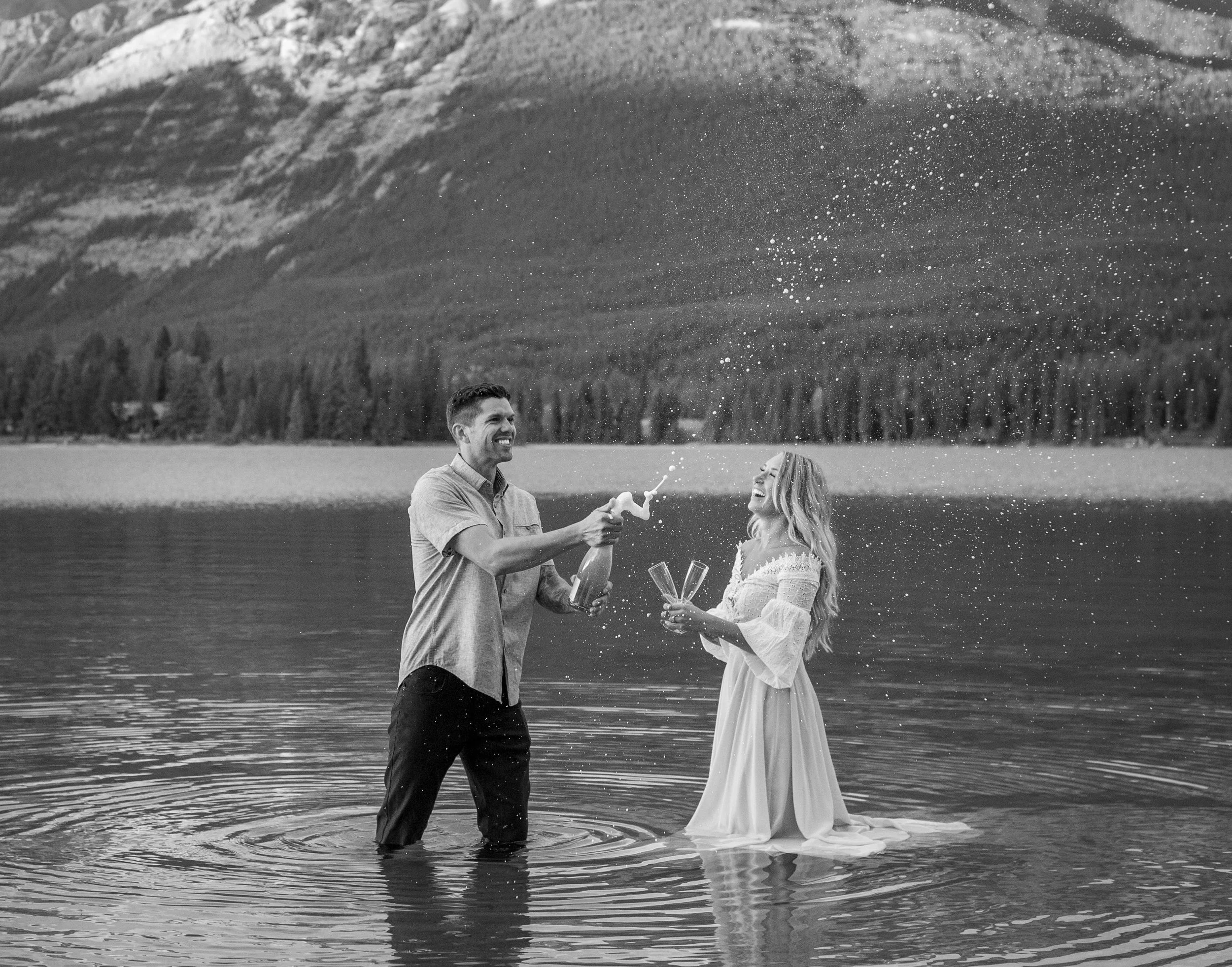 A couple popping champagne on their elopement in Jasper National Park, photo by Jasper elopement photographer Megan Posein