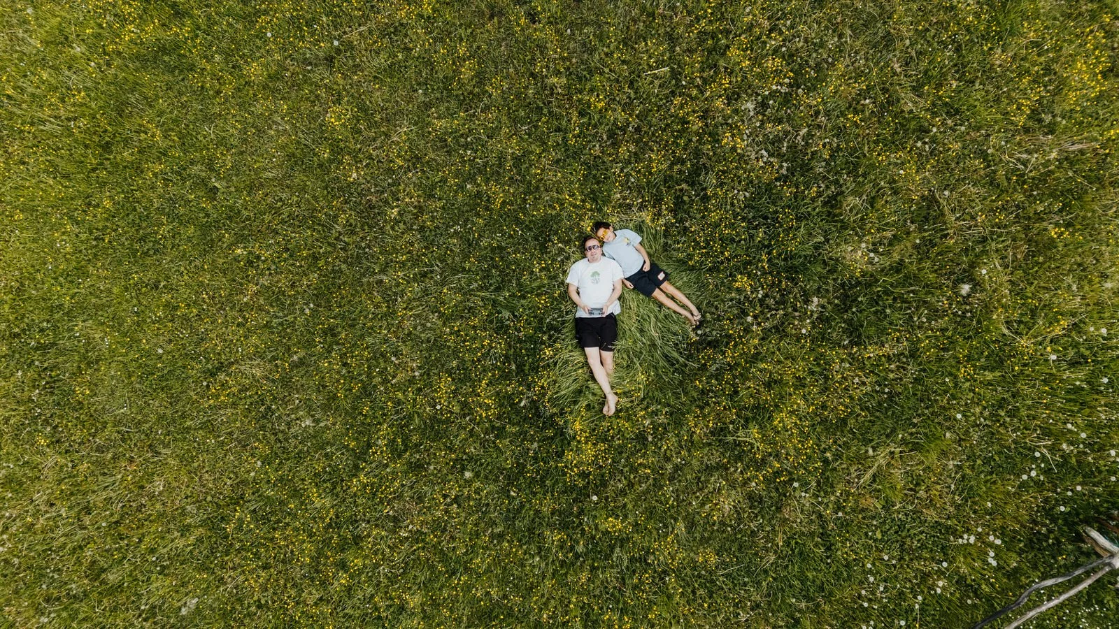 Two people lying on a grassy field with small yellow flowers, captured from above.