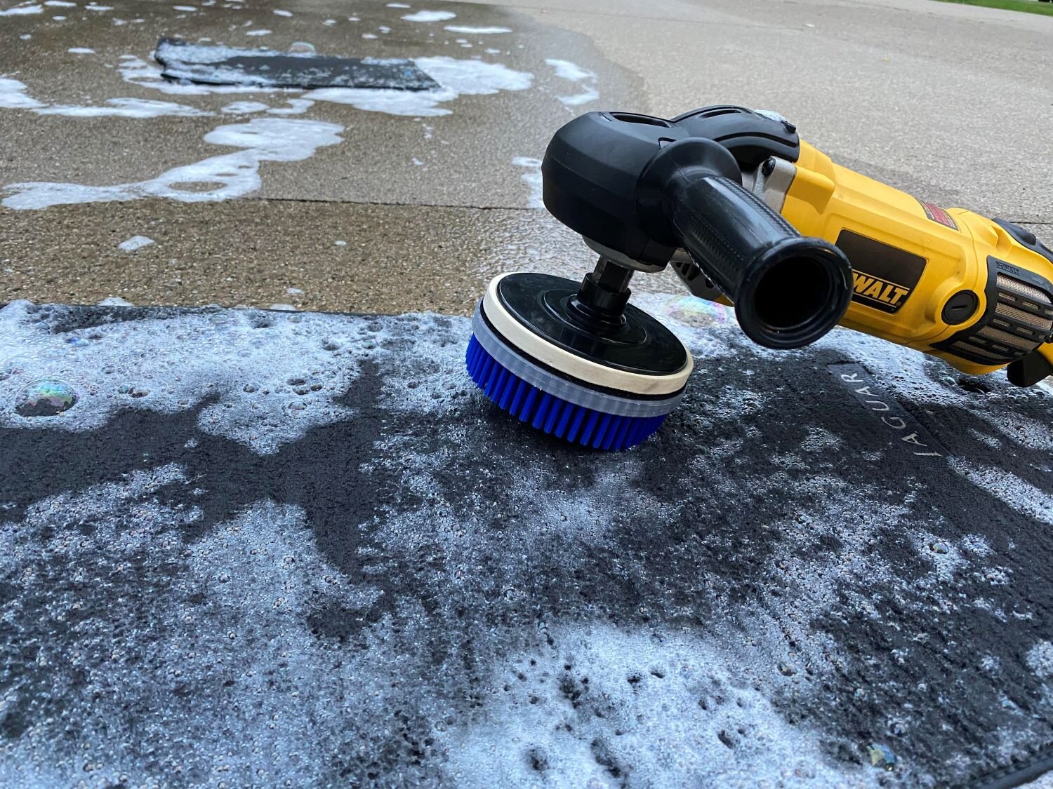 Agitation is being performed to loosen hard and embedded dirt before pressure washing of floor mats.