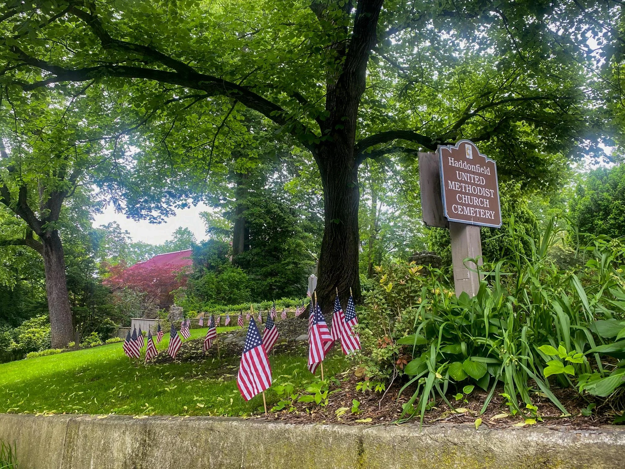 Haddonfield United Methodist Cemetery Sign at entrance of cemetery with US flags on the lawn.