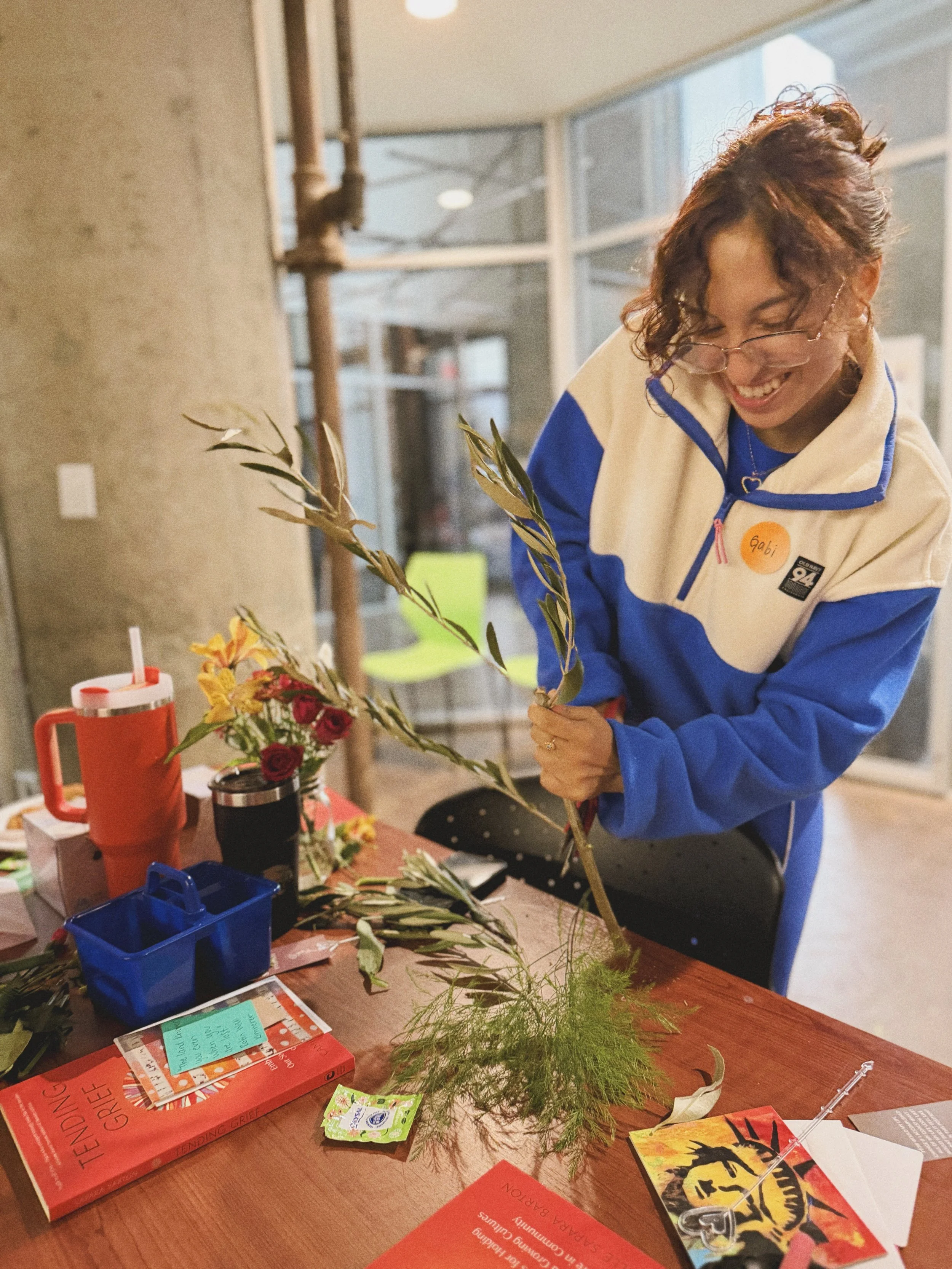 A woman with curly hair and glasses arranging flowers on a table in a bright room.