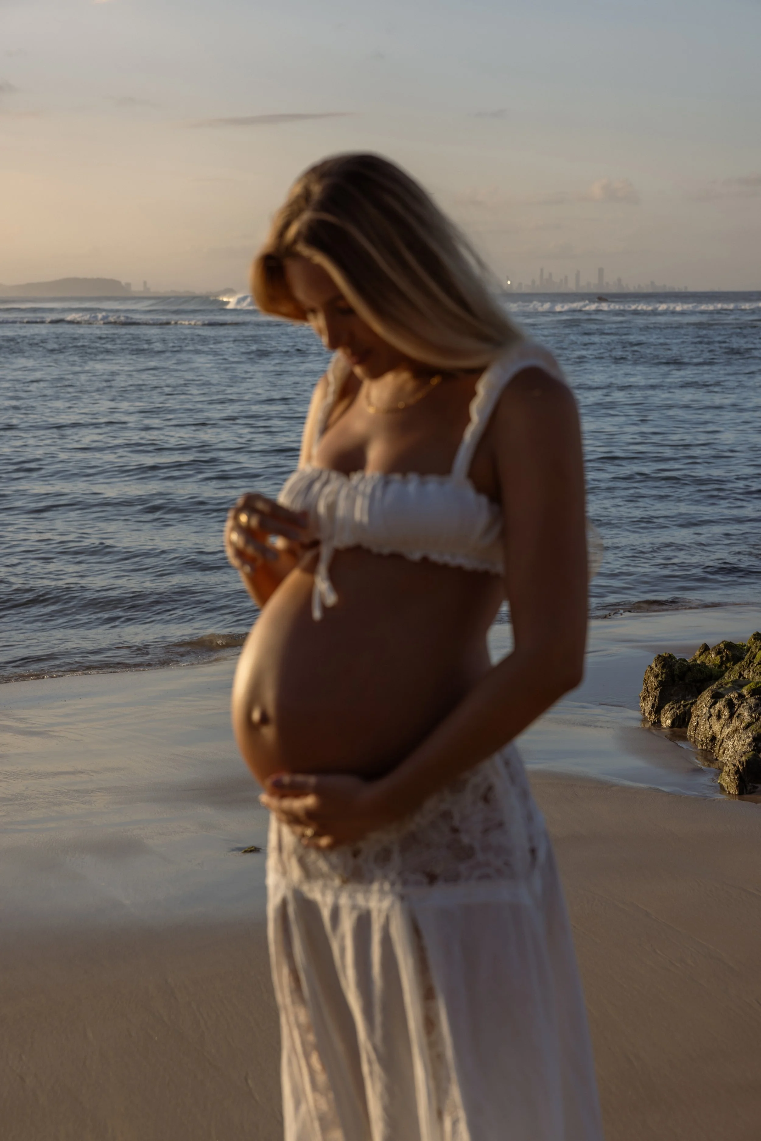 Pregnant woman in soft natural light, minimal and editorial maternity photography capturing a quiet, emotional moment.