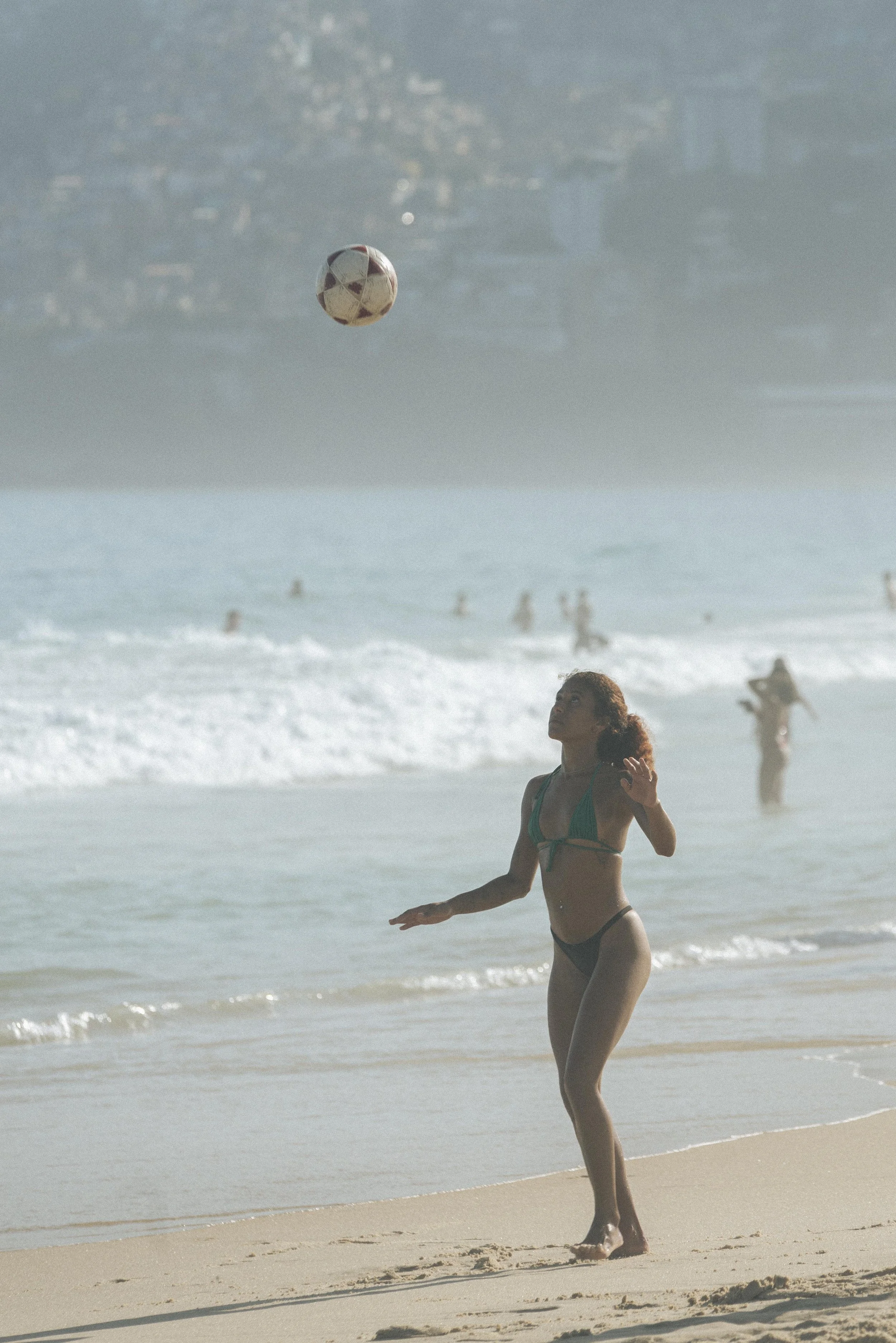 Person in swimsuit playing with a ball on the beach, ocean in background.